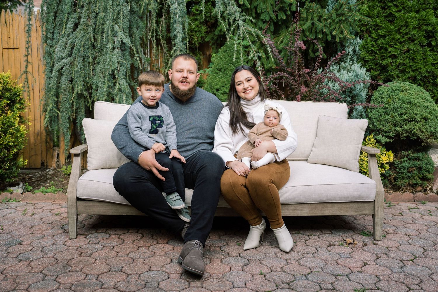 A family relaxing together on an outdoor sofa in a beautifully landscaped garden.