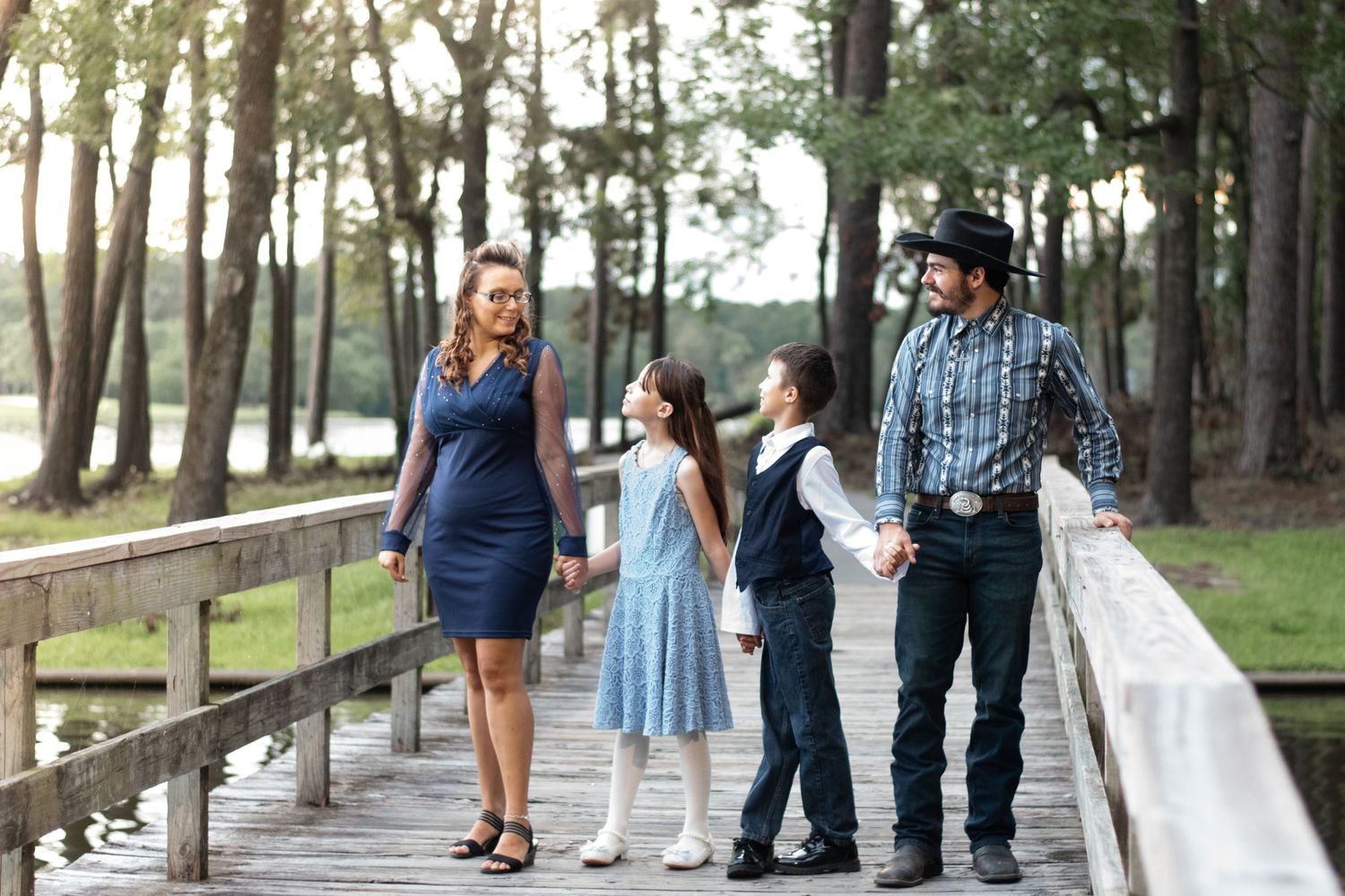 Family standing together on wooden boardwalk in wooded setting at sunset.