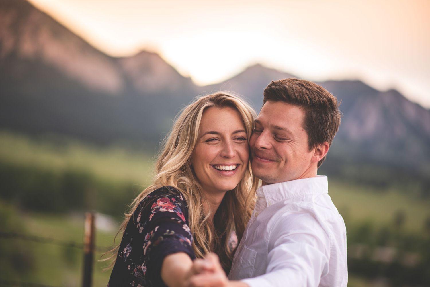 Couple embraces during sunset with mountain peaks in the background.