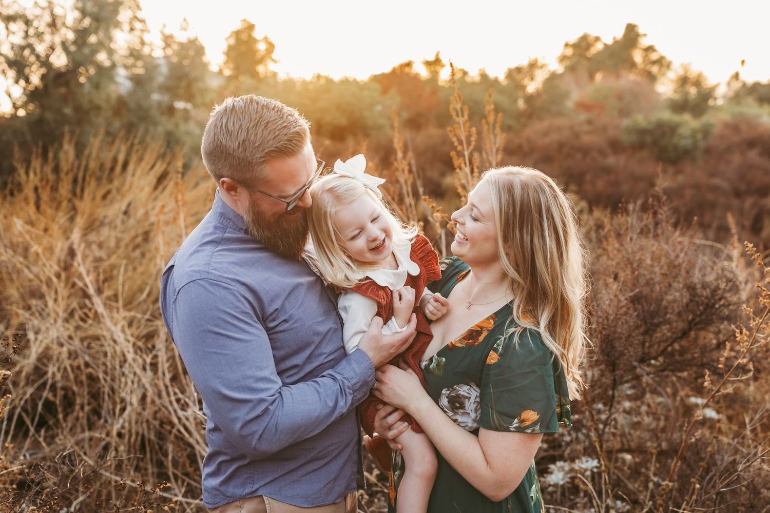A family shares a tender moment together at sunset in a field of golden grass.