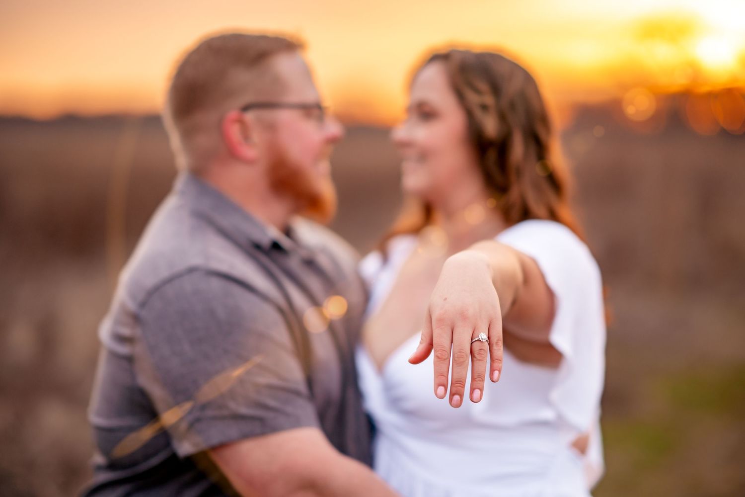 A newly engaged couple showing off an engagement ring during golden hour sunset.