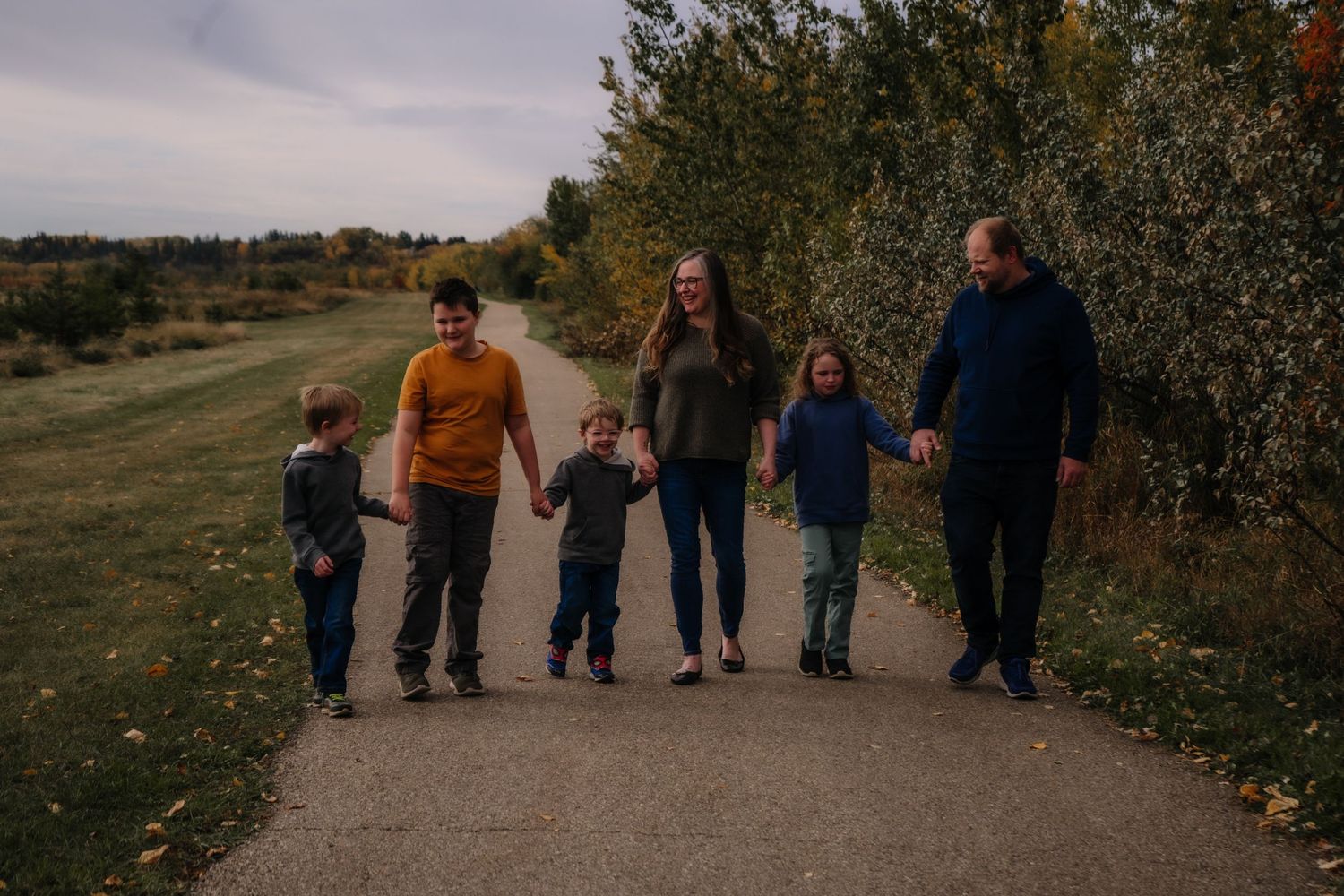 Multi-generational family holding hands while walking on path during sunset.