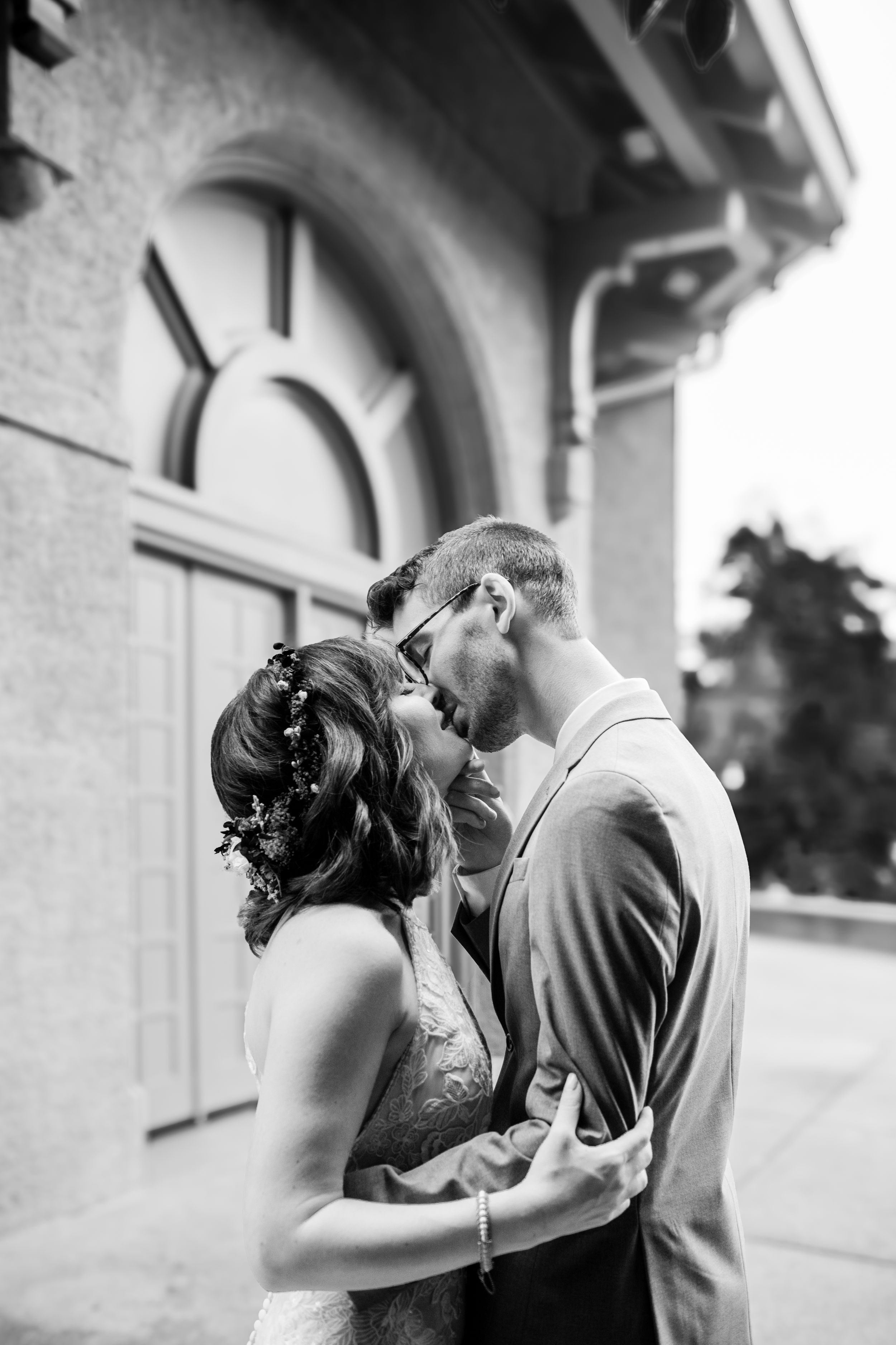 A romantic black and white wedding photo showing a tender kiss in front of an arched doorway.