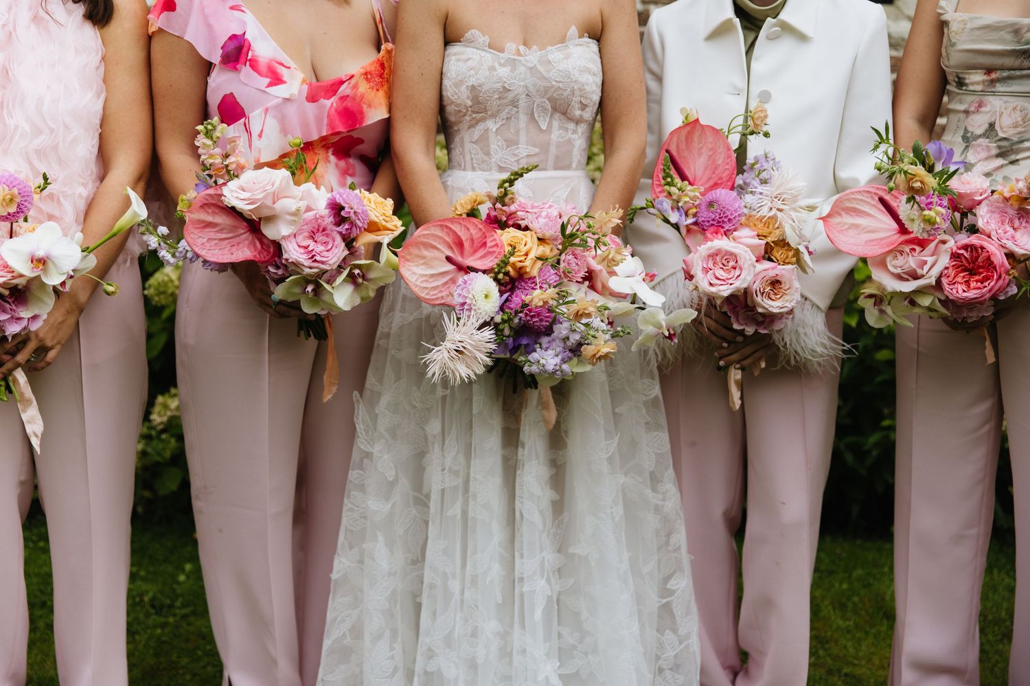 Beautiful pink and coral floral bouquets held against blush bridesmaid dresses and a white wedding gown.