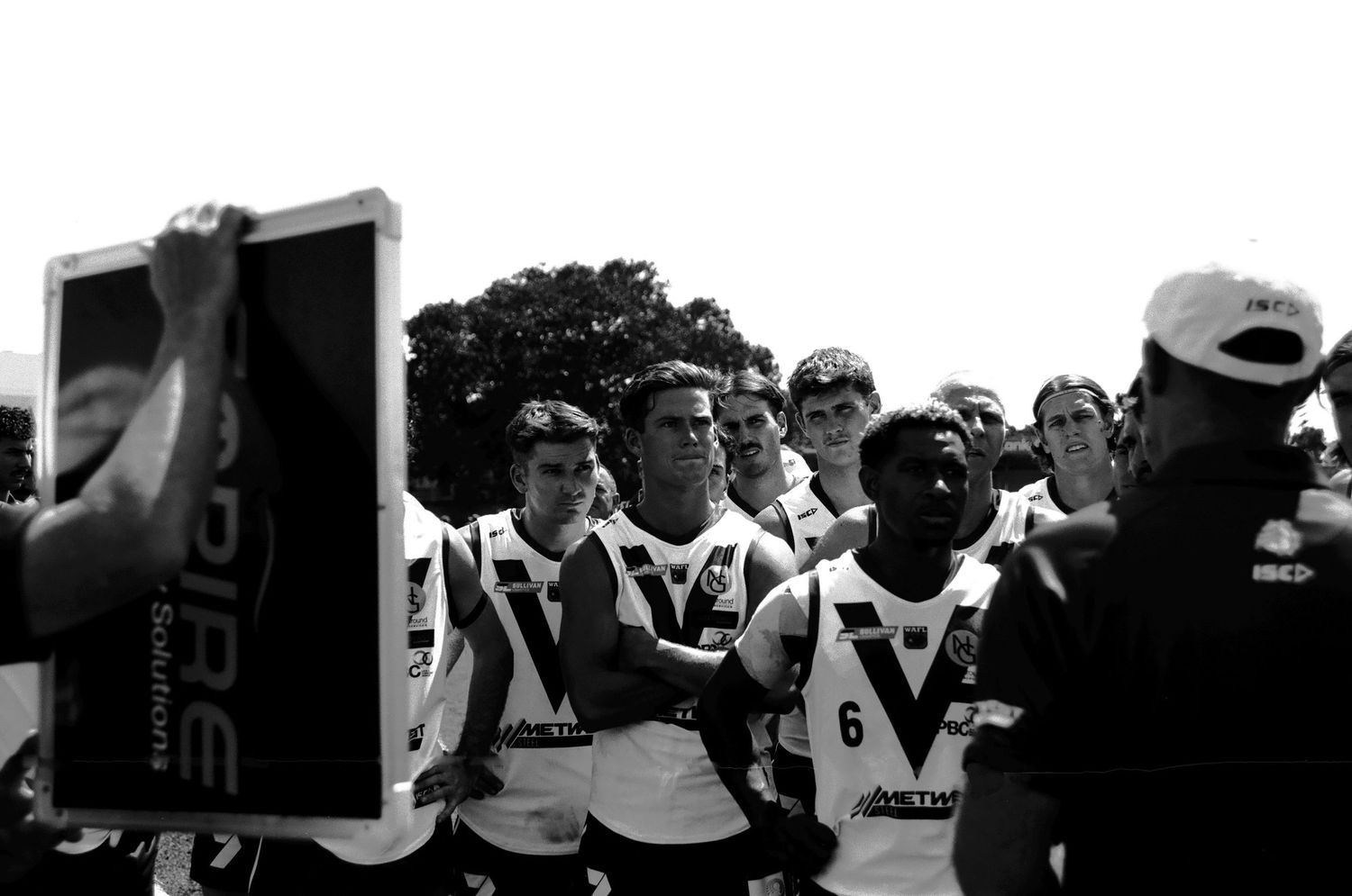 Group of athletes huddled together on field in black and white.
