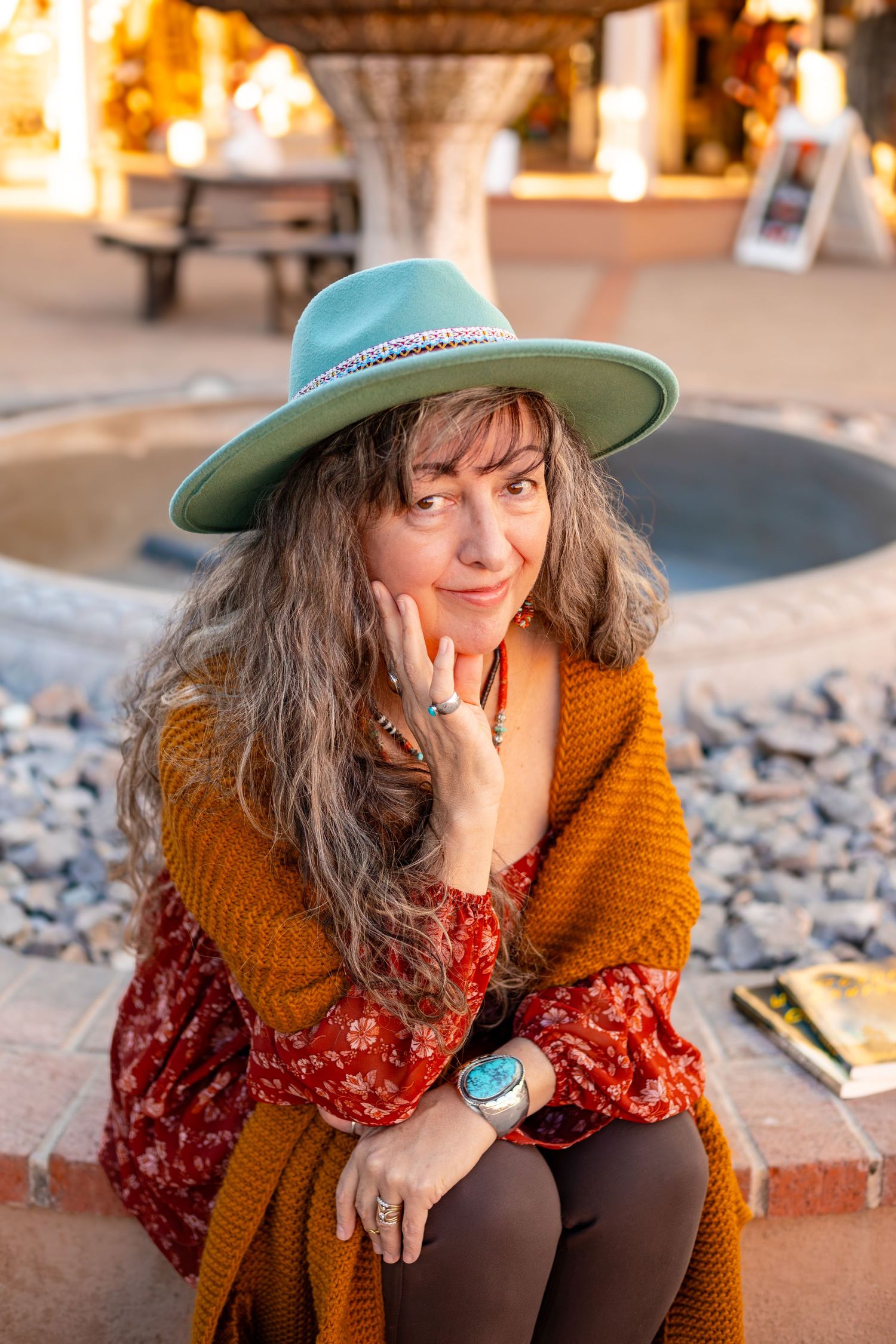 A cozy autumn portrait featuring mustard cardigan, red floral dress, and teal hat on rustic stone steps.
