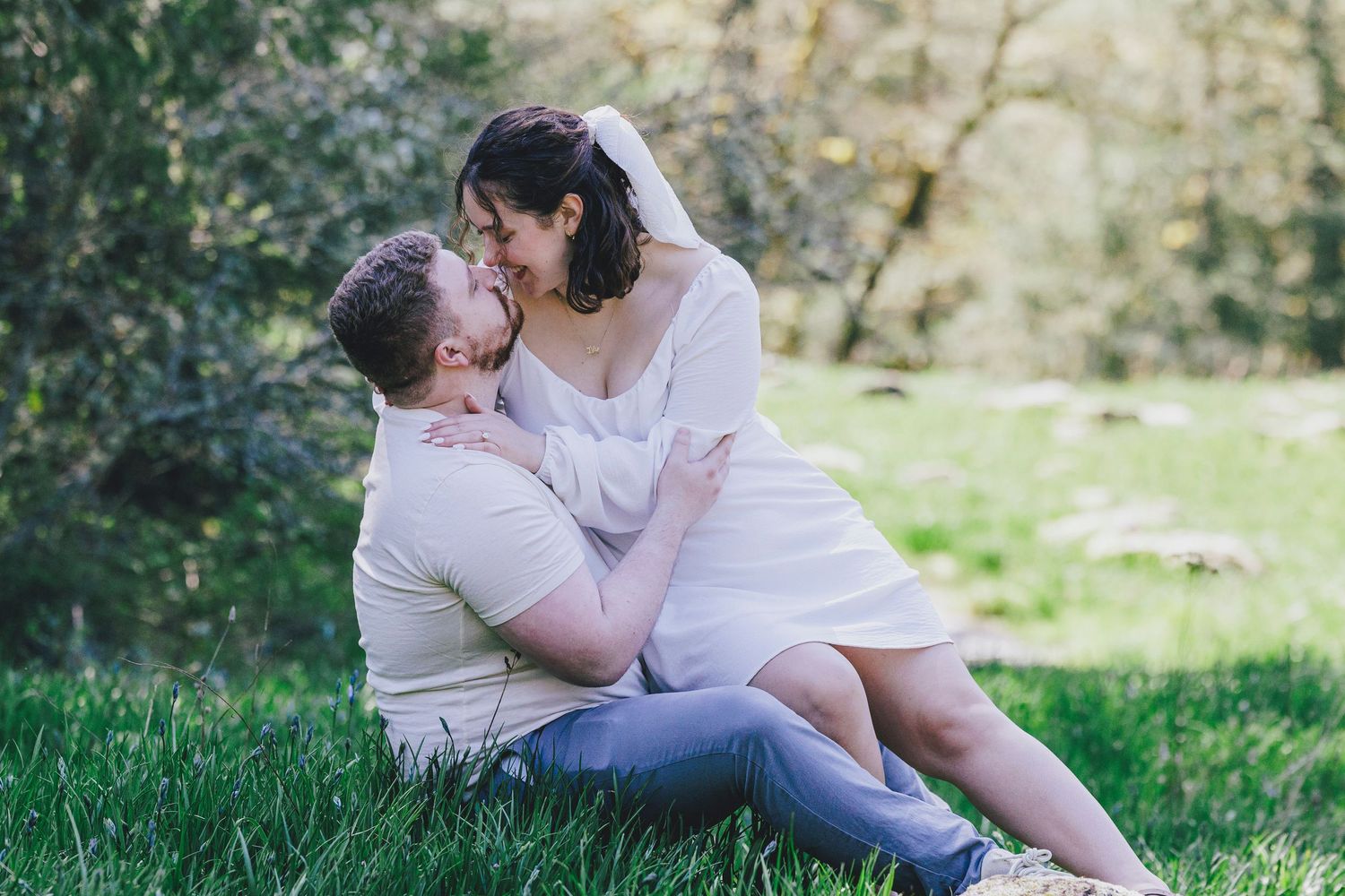 A tender moment shared between a couple on green grass during a sunny outdoor photoshoot.
