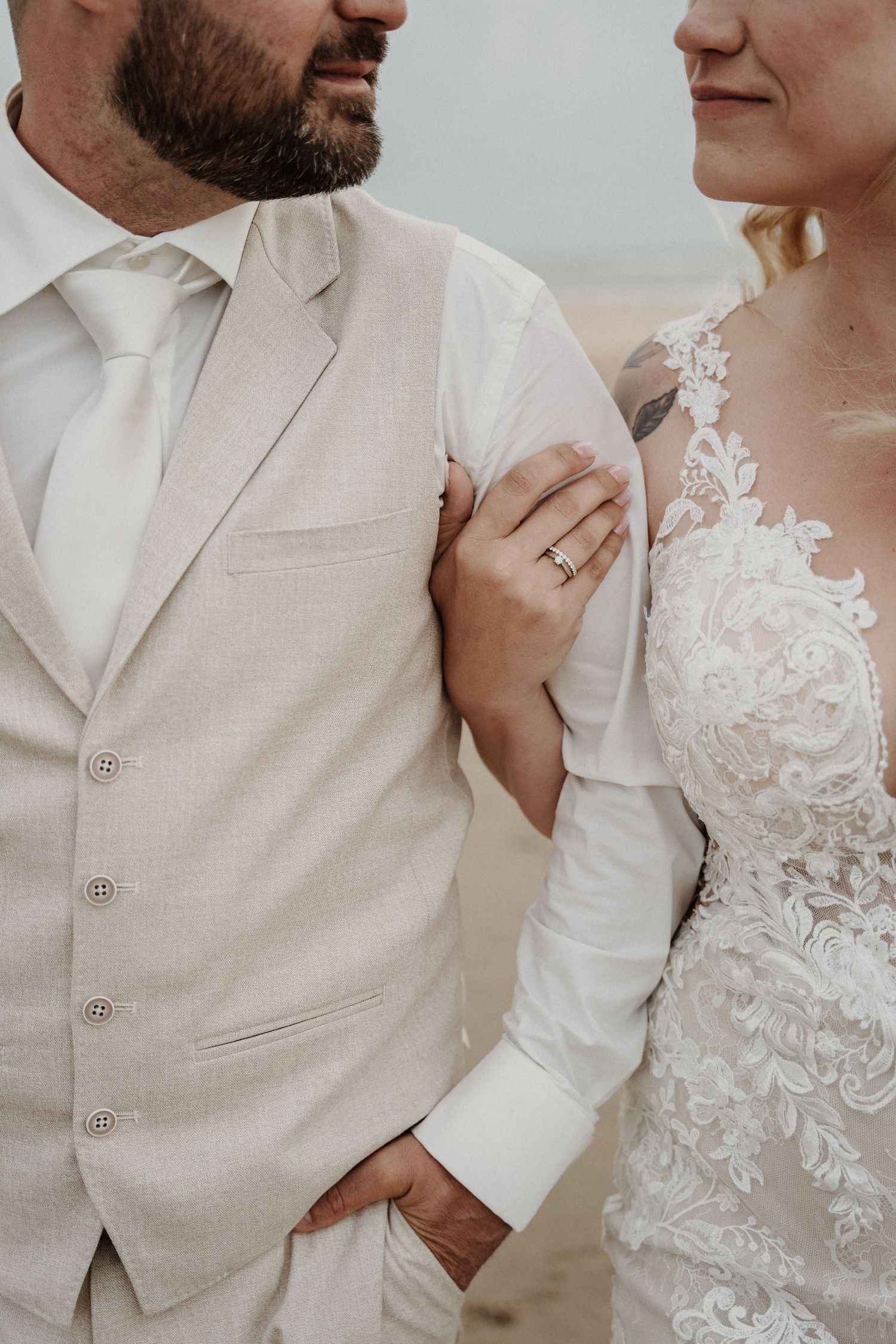 Close-up of newlyweds in beige suit and white lace wedding dress showing romantic details of their attire.