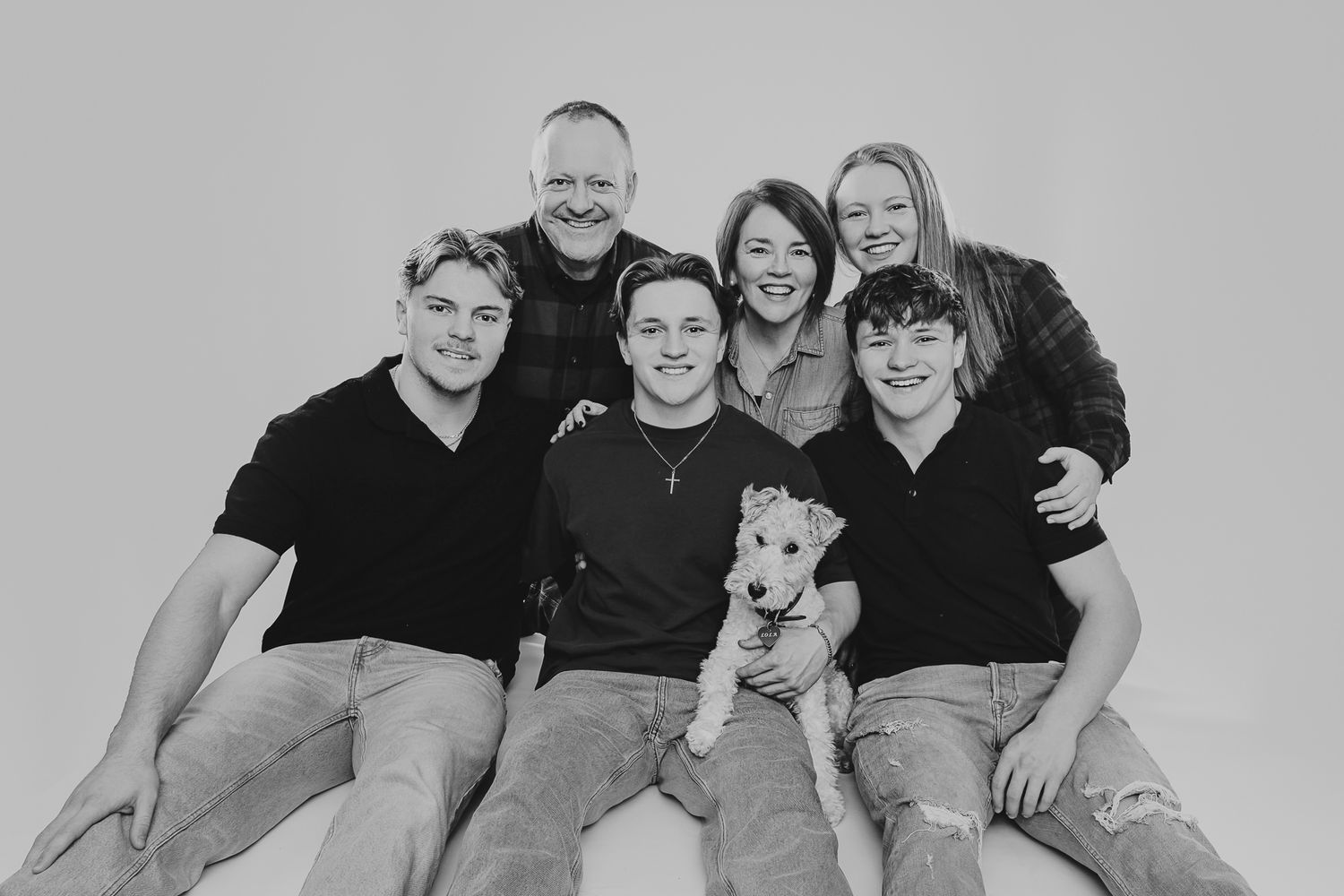 A casual family portrait featuring several people in black shirts with their dog.