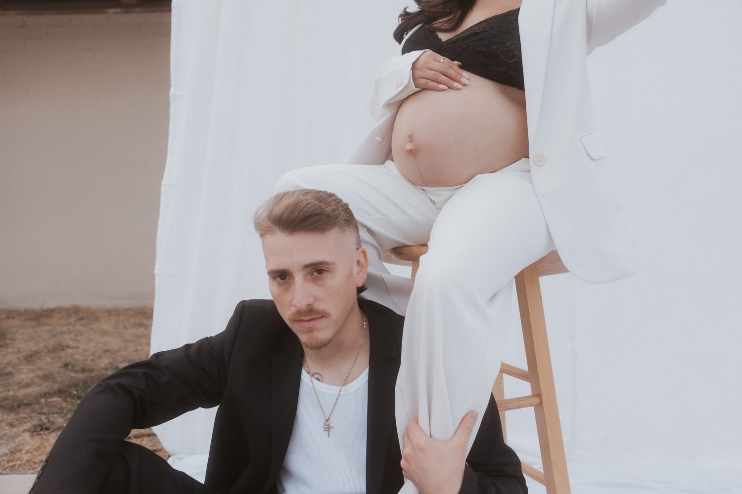 Maternity photoshoot with couple in black and white outfits against neutral backdrop.
