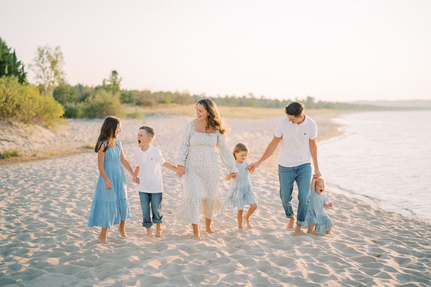 A family walking together on a sandy beach at sunset wearing coordinating blue and white outfits.