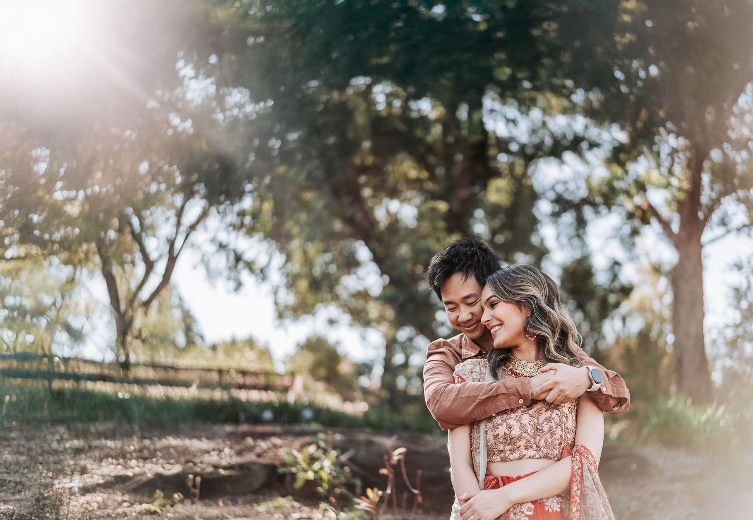 A couple embraces outdoors in a dreamy sunlit park setting with natural greenery in the background.