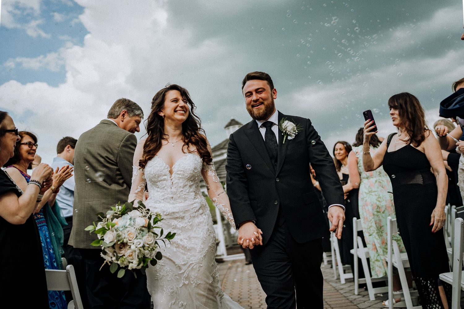 A couple shares their first kiss during a rooftop wedding ceremony with guests and a gazebo in the background.