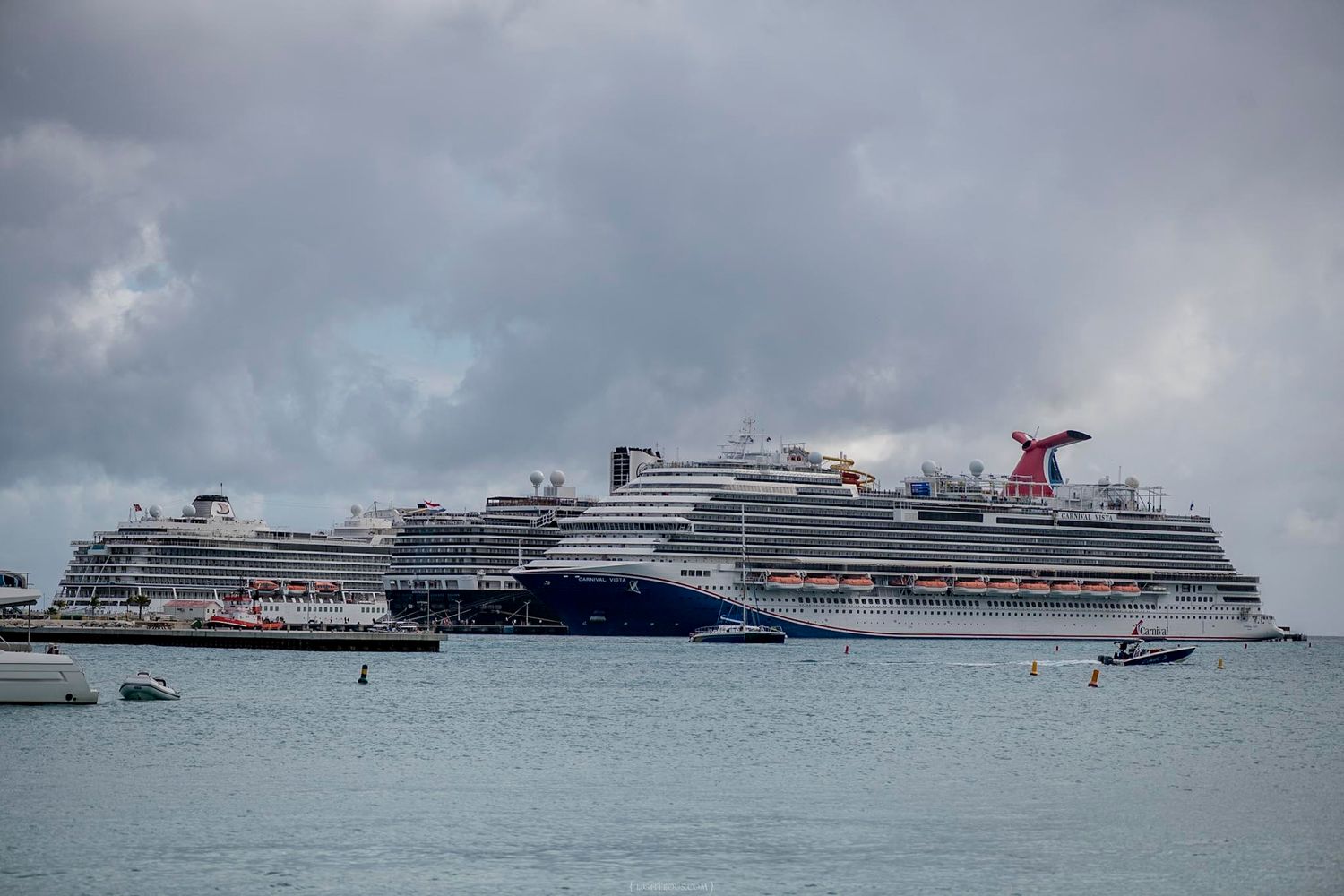 Two large Holland America Line cruise ships docked at a tropical port with turquoise water and blue skies.