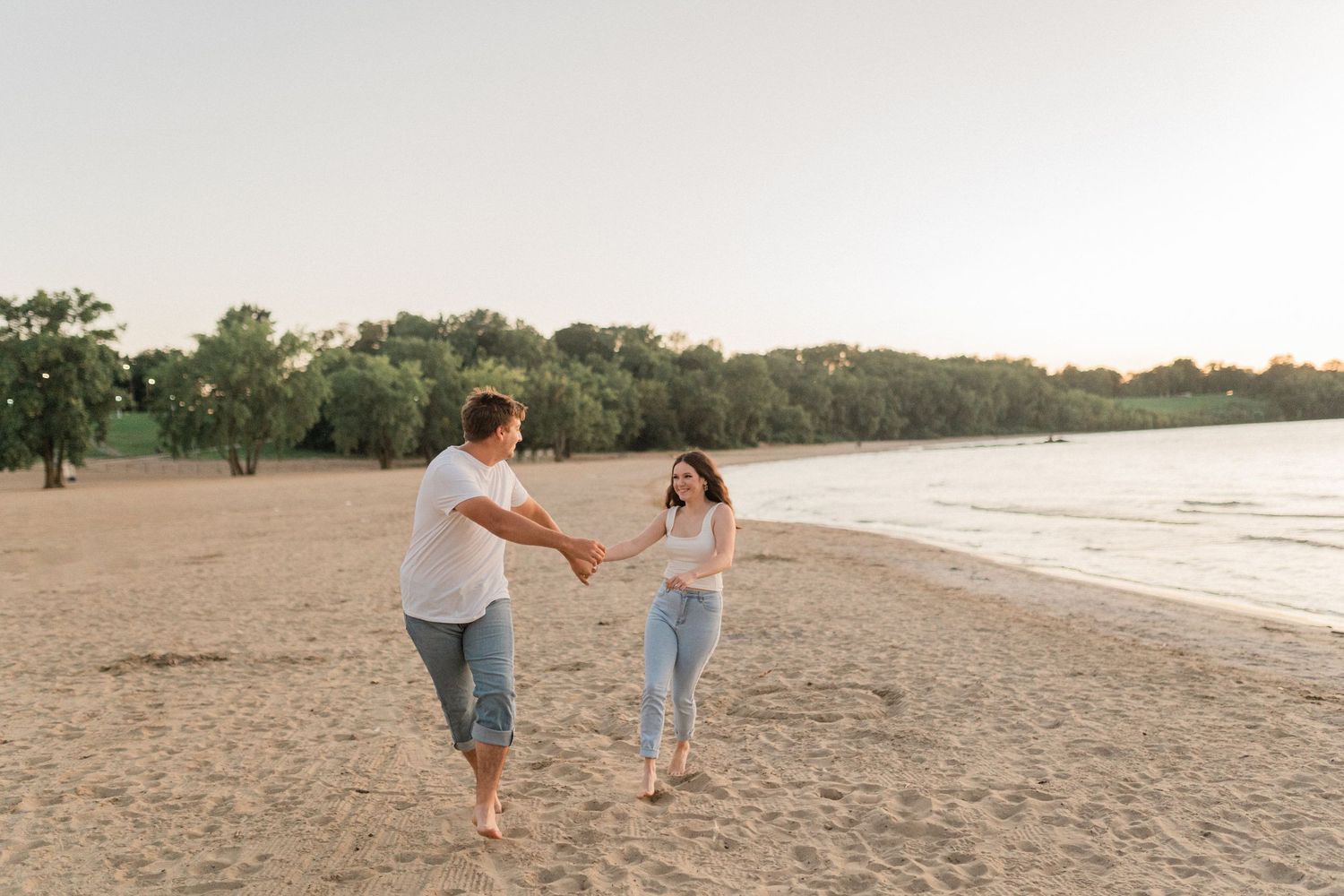 Two people walk hand in hand along a sandy beach at sunset with ocean waves in the background.