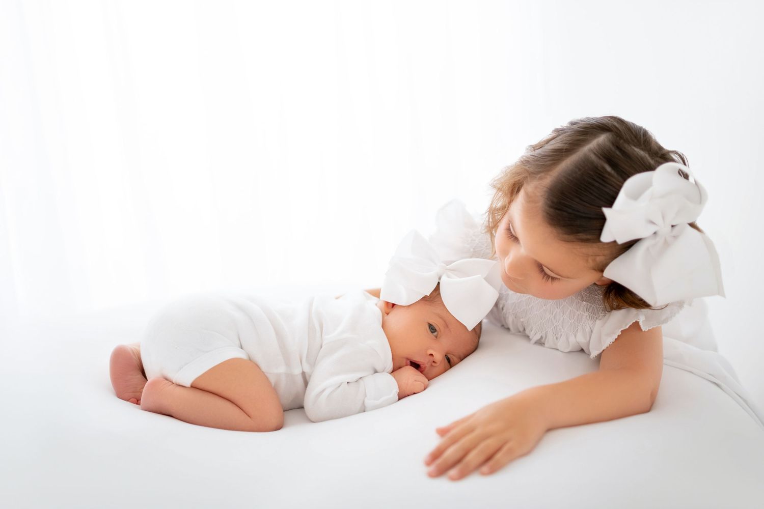 Big sister kissing newborn baby girl during timeless sibling newborn photography session in Winchester VA studio