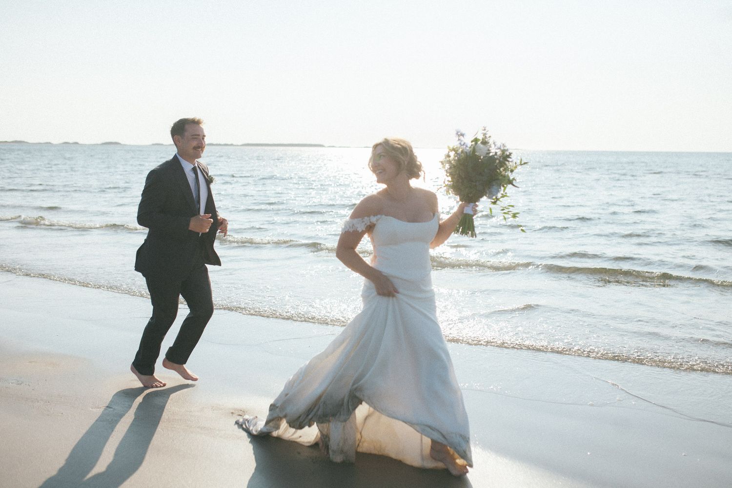 bride and groom run through the shallow waves on Chesterman Beach in Tofino laughing