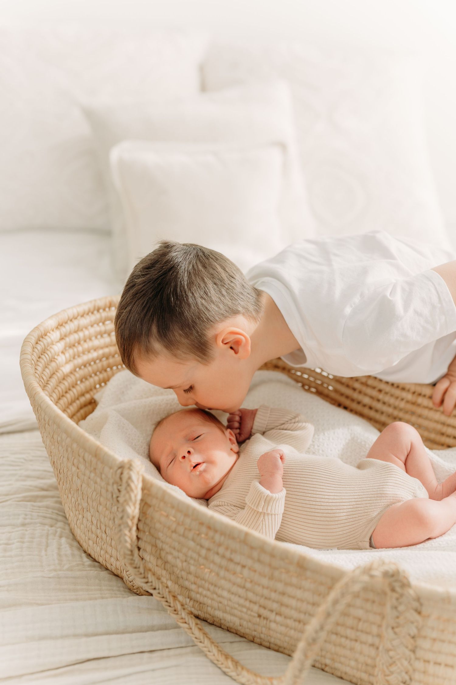 Grand frère donnant un baiser sur le front de son nouveau petit frère lors d’une séance nouveau-né en famille au studio près de Québec
