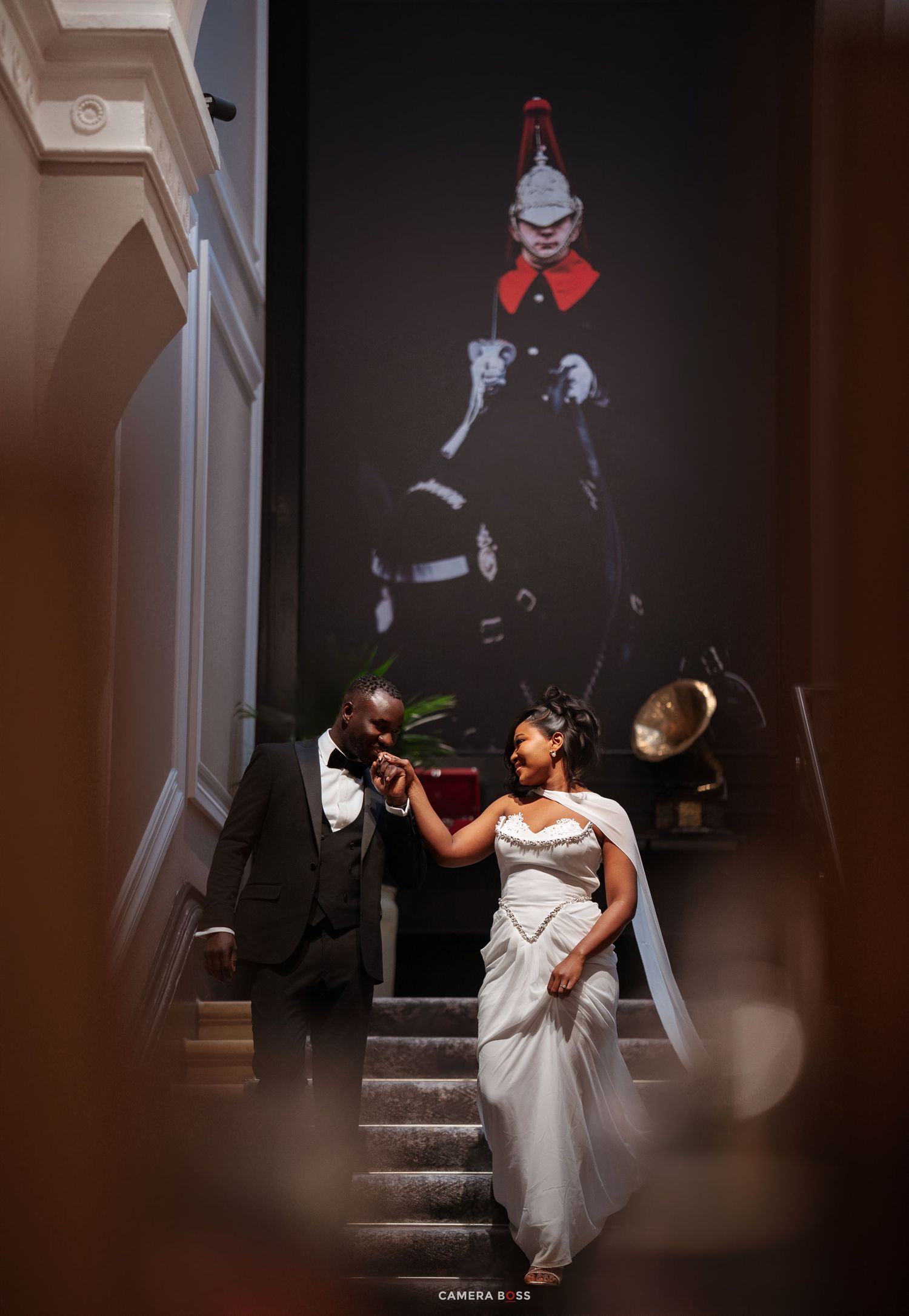 Bride and groom share a romantic moment on elegant staircase, with a dramatic equestrian mural backdrop at their wedding venue.