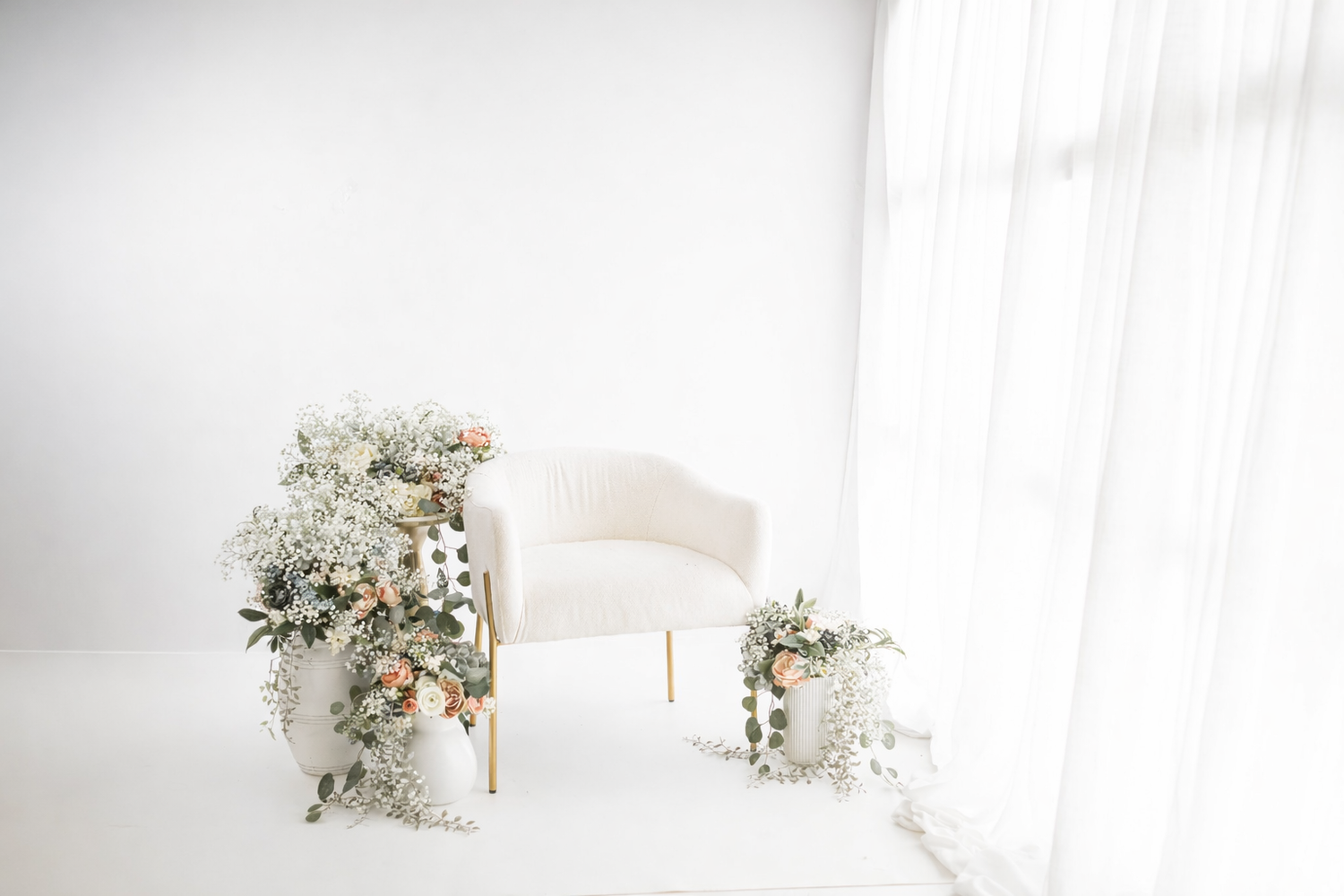 Two people in black and beige outfits pose together against a floral backdrop with blue and pink roses and baby's breath.