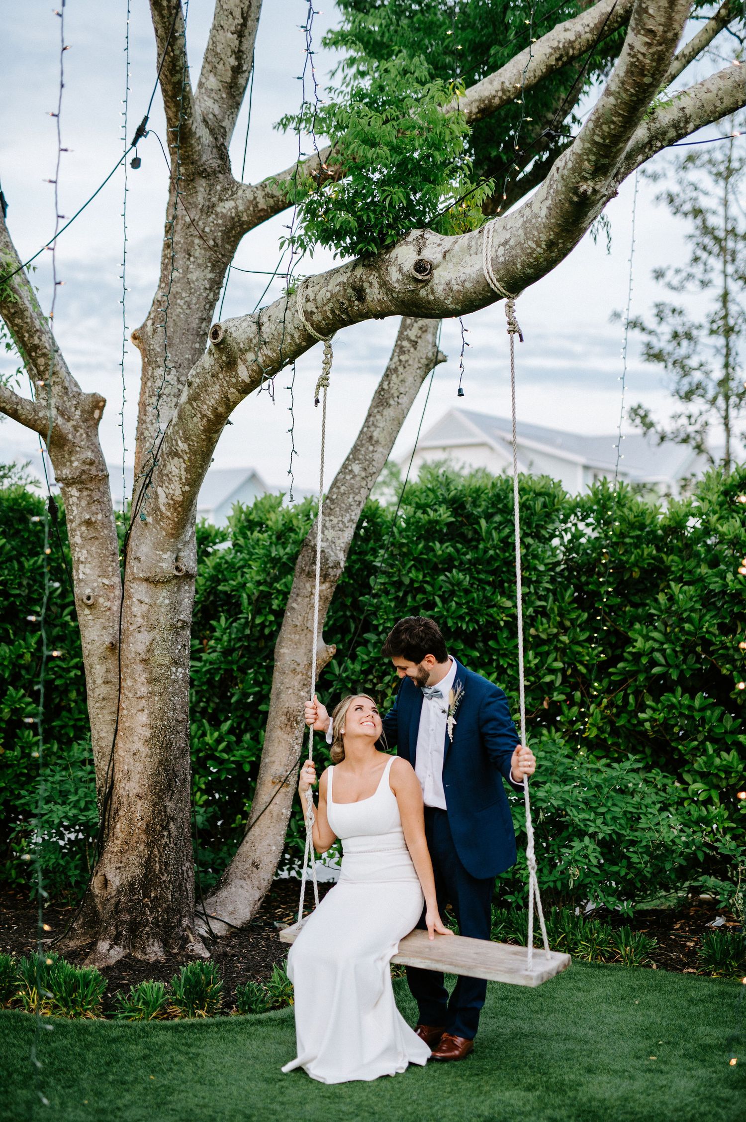 A couple sits together on a rustic tree swing in a lush garden setting during their wedding celebration.