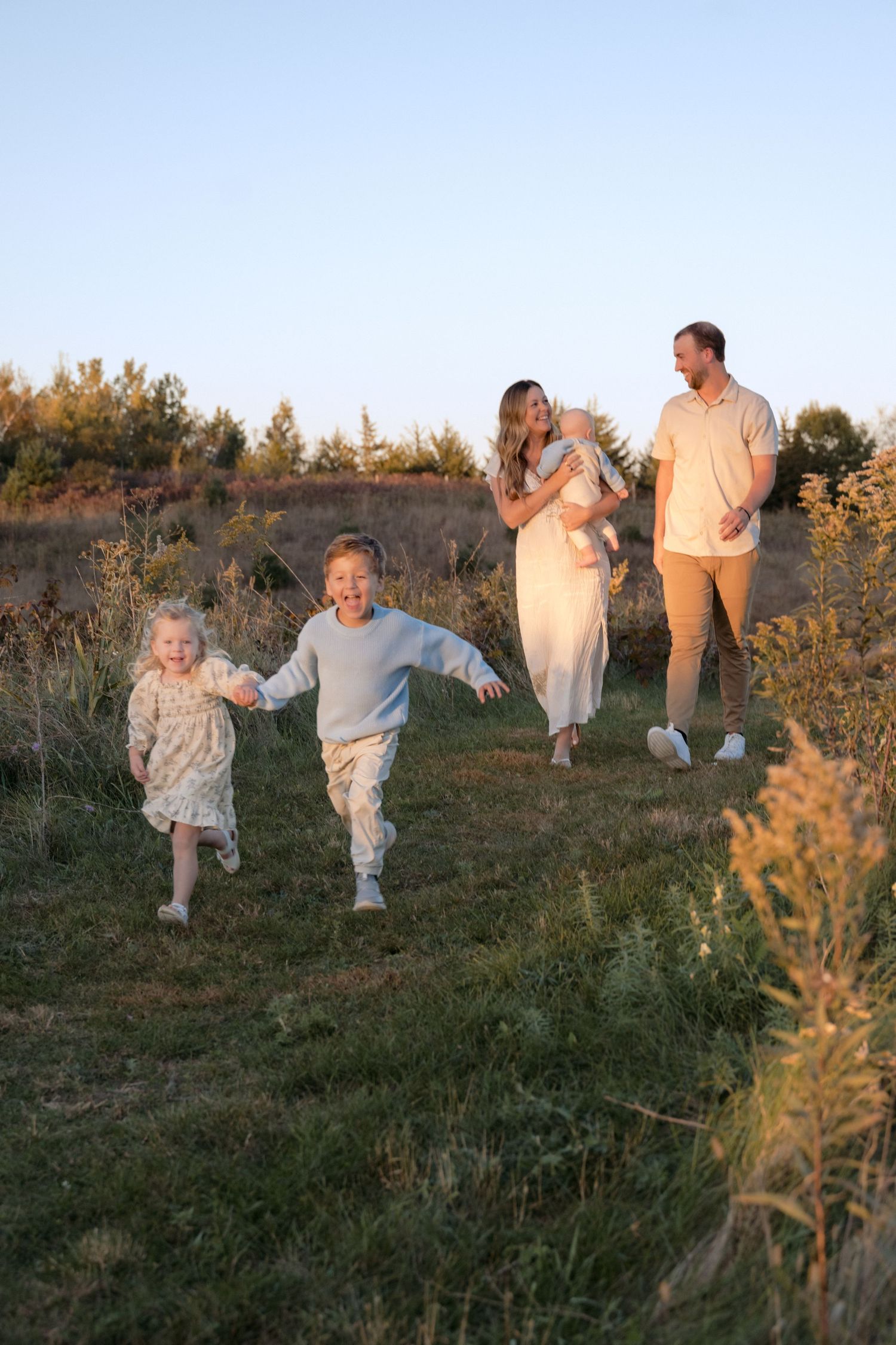 young kids running through the grasses while parents and baby follow behind during fall mini session in hudson wisconsin