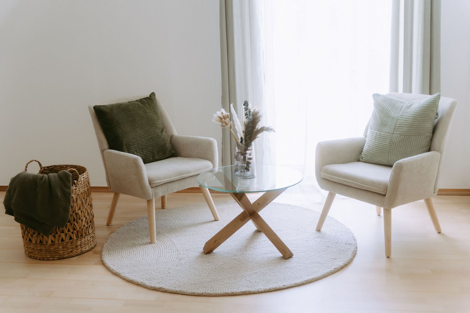 Two beige armchairs with a glass coffee table on a round rug in a bright, minimalist living room.
