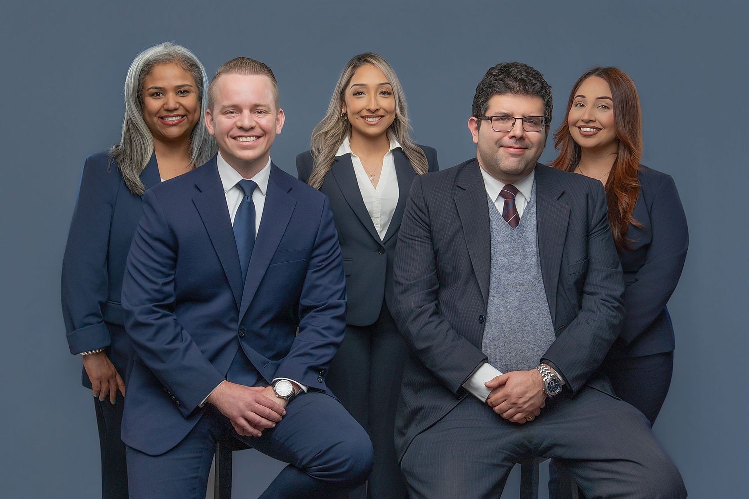 Five professional business team members in suits posing together for a formal corporate group portrait photo.
