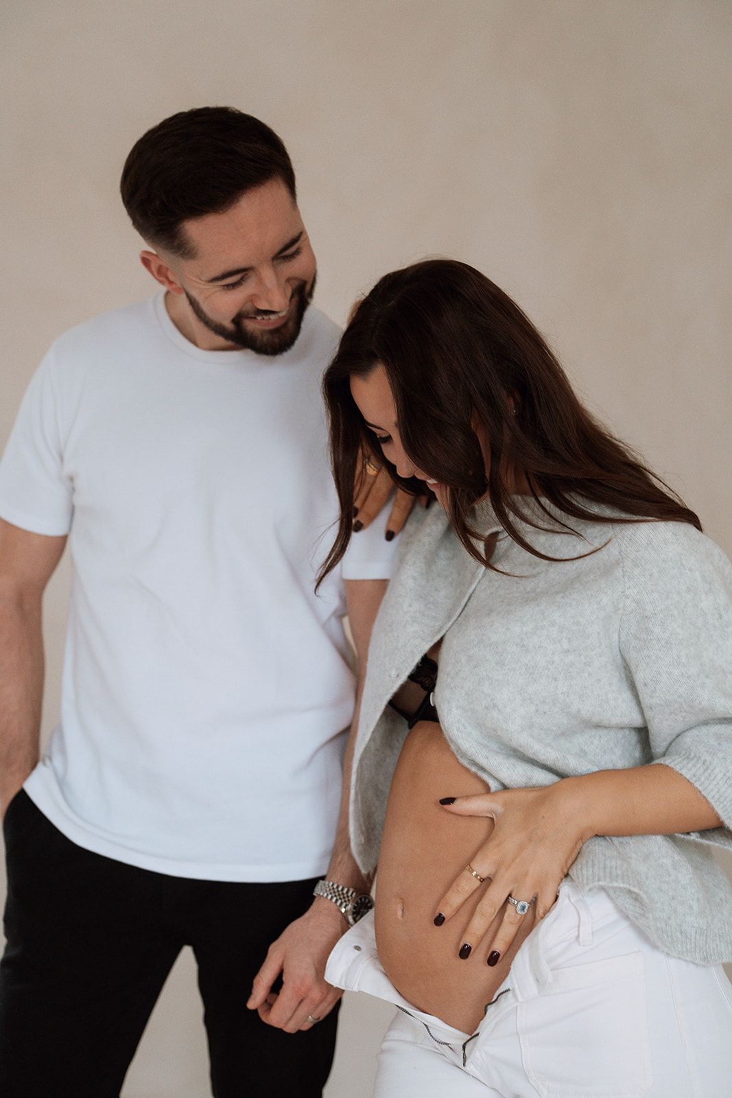 A couple in white clothing embraces while showing off an ultrasound photo in a pregnancy announcement photoshoot.