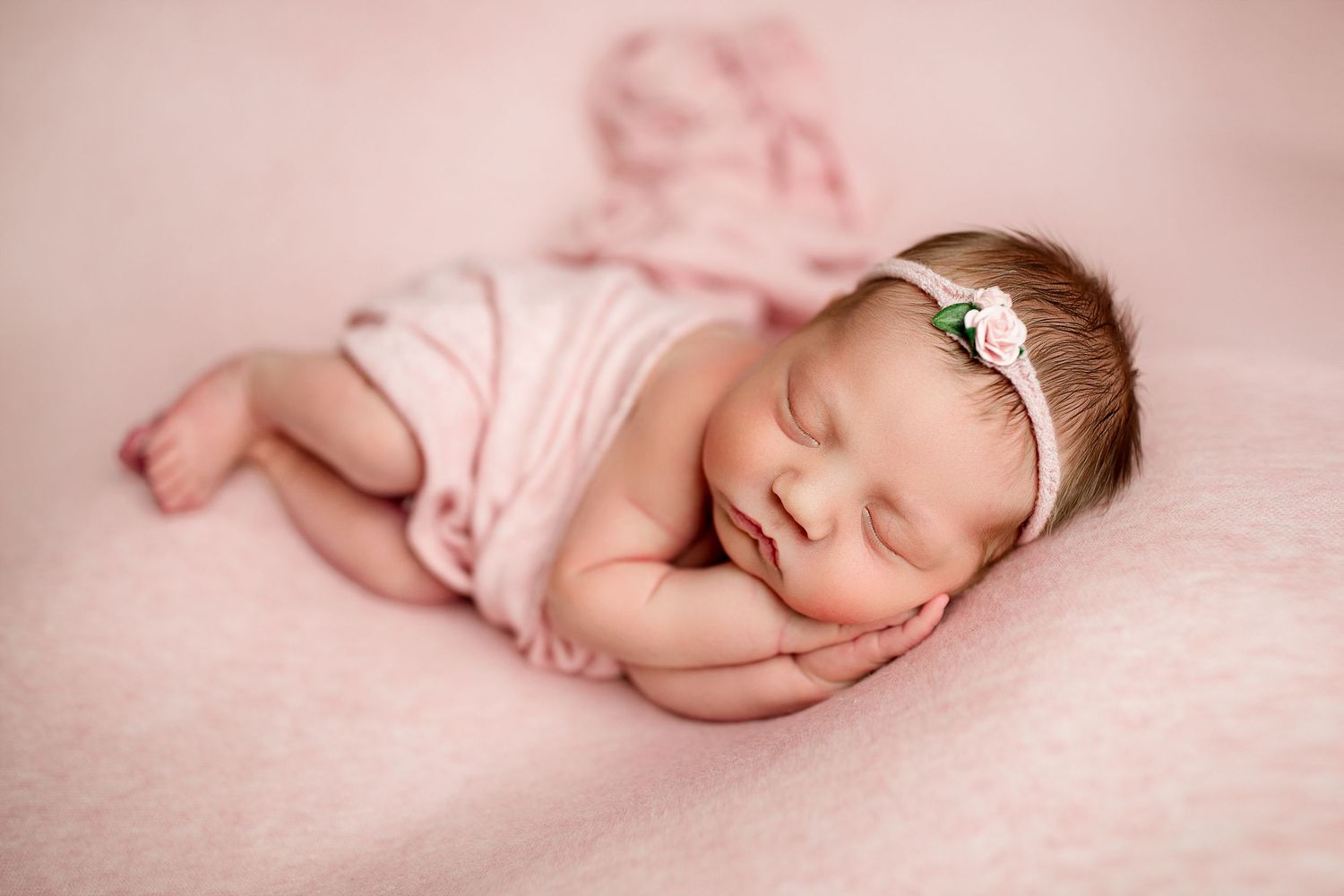 Sleeping newborn baby in pink swaddle blanket on soft textured backdrop.