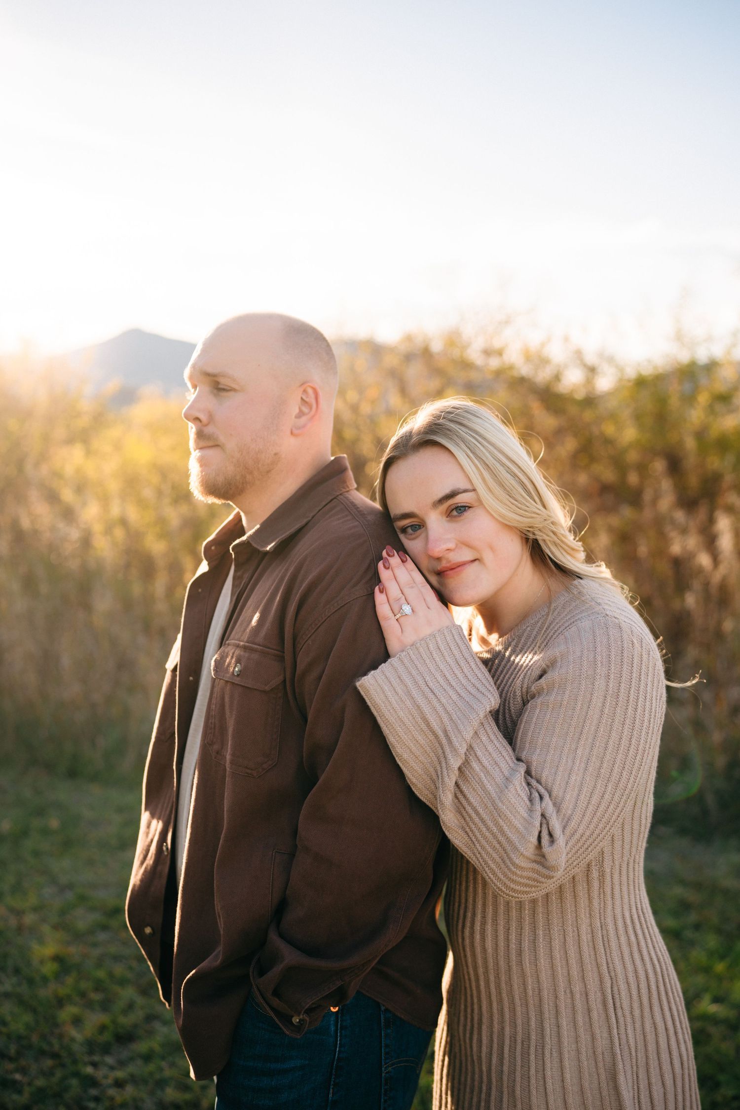Romantic couple embraces outdoors during golden hour in a natural setting with sunlit foliage in background.