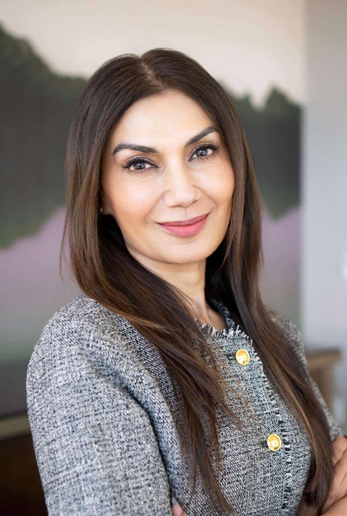 Professional headshot of a woman with long dark hair wearing a gray tweed blazer, smiling confidently.