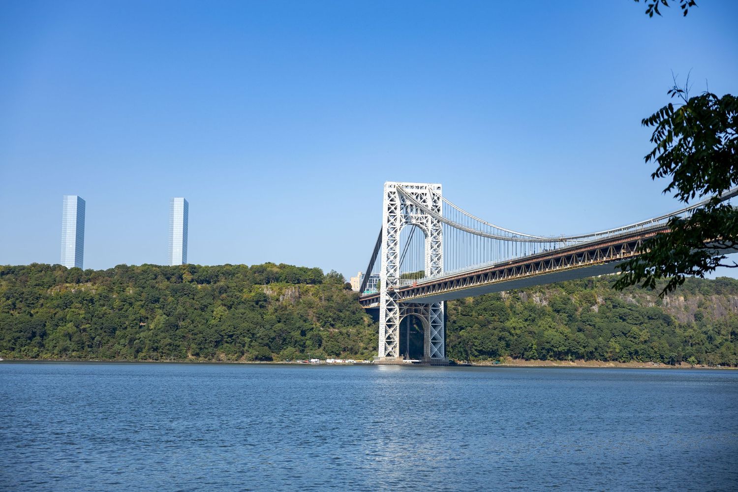 George Washington Bridge spanning the Hudson River with lush green hills and blue sky in New York.