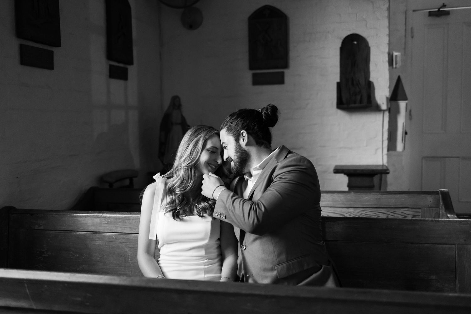 A person in a wedding dress sitting alone in a church pew near sunlit windows.