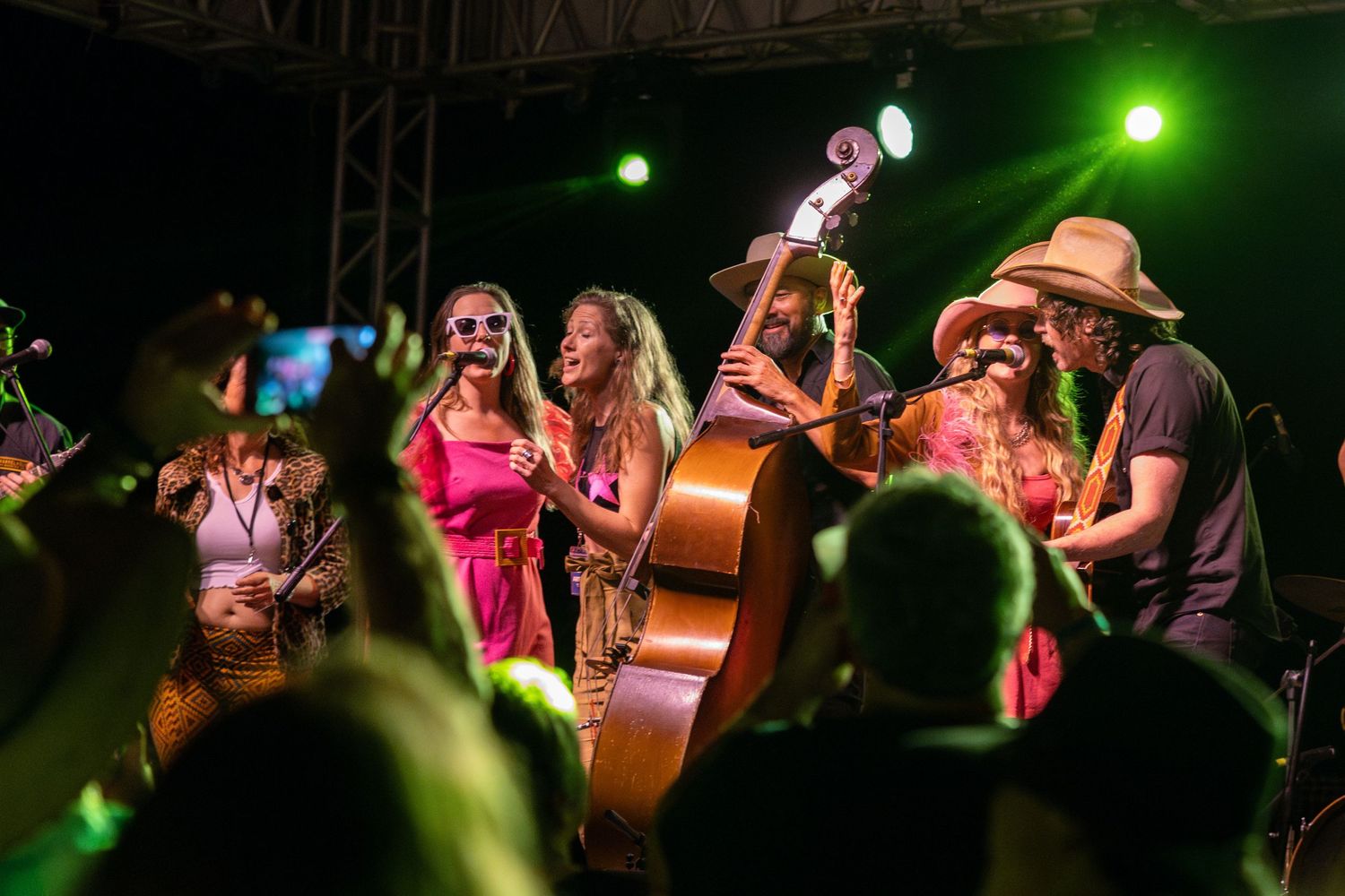 Musicians perform energetically on stage with instruments including upright bass under green stage lighting at night.