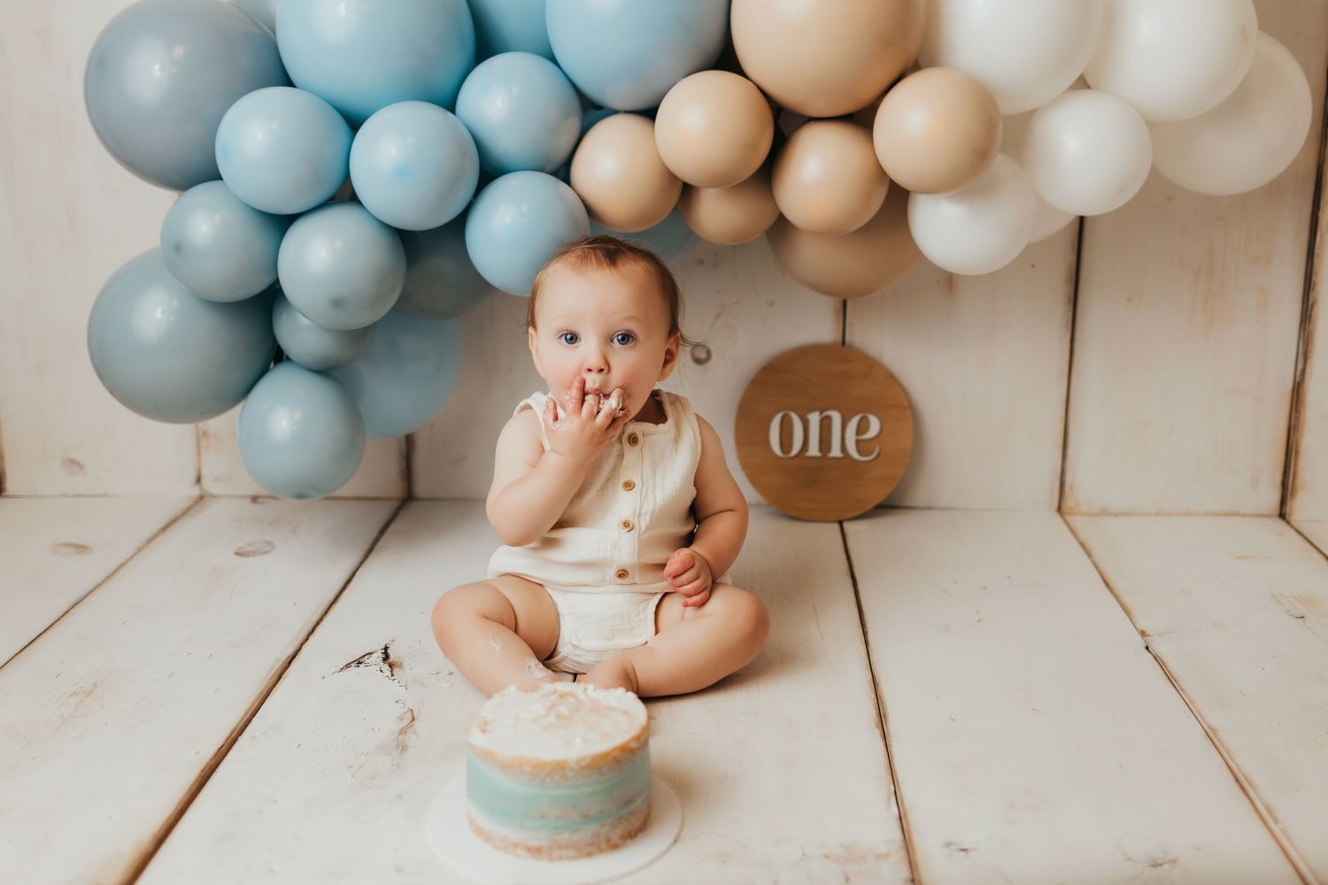Baby's first birthday cake smash setup with blue and neutral balloon arch decoration.