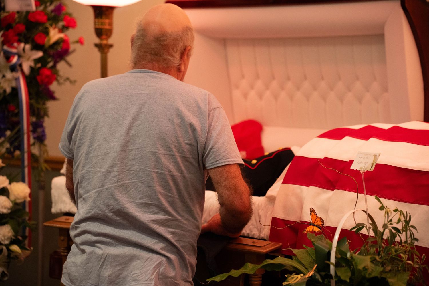 Person kneeling beside flag-draped casket in solemn moment.