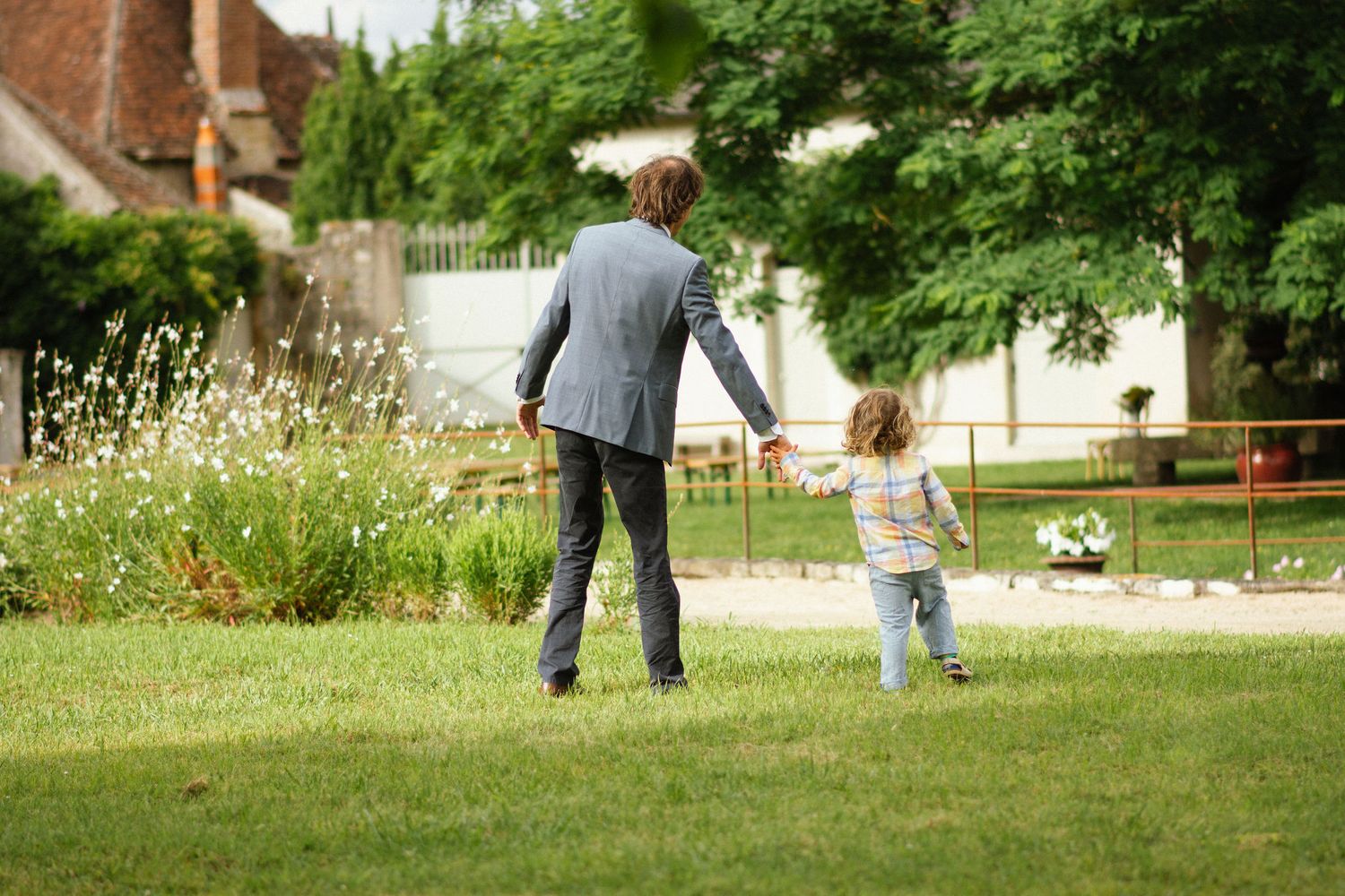 Un père et son enfant main dans la main, marchant dans un jardin — un instant de lien et de douceur capturé en toute simplicité.