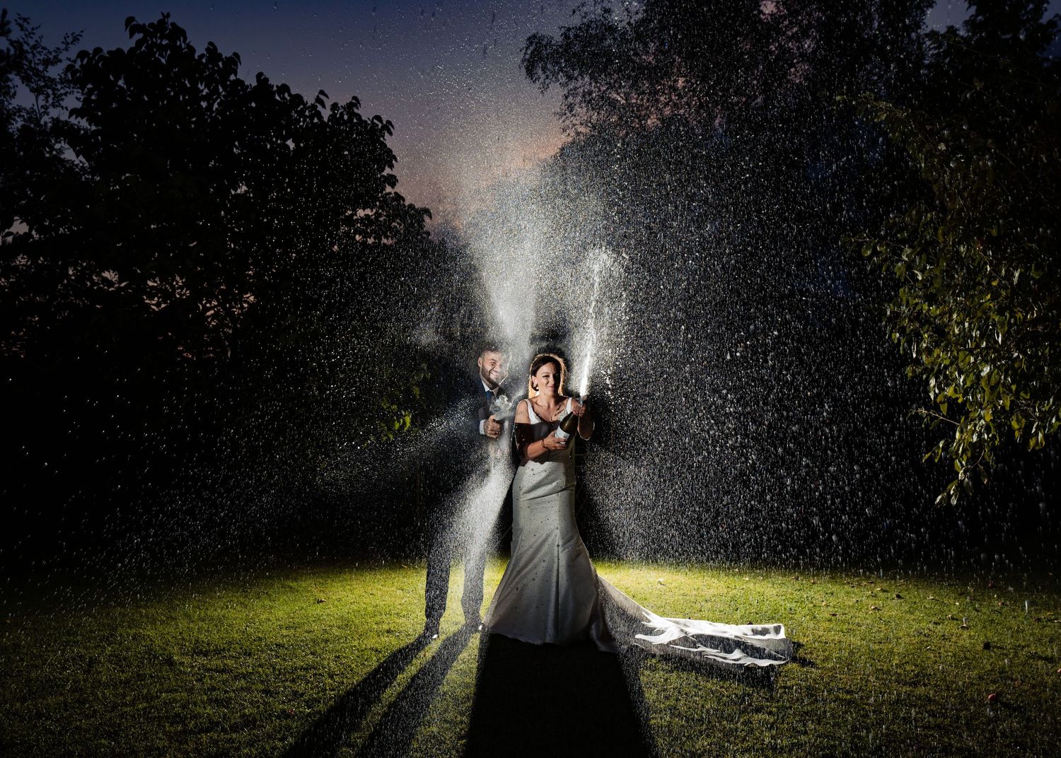 A couple illuminated with a backlight while spraying champagne in celebration of their wedding day in Nova Scotia.