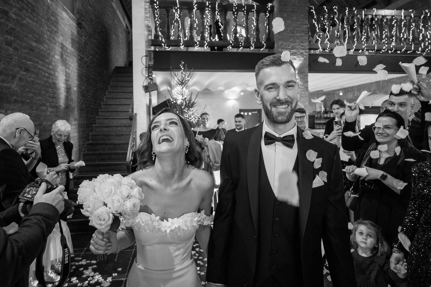 Black and white photo of a happy bride and groom laughing with wedding guests holding sparklers at celebration.