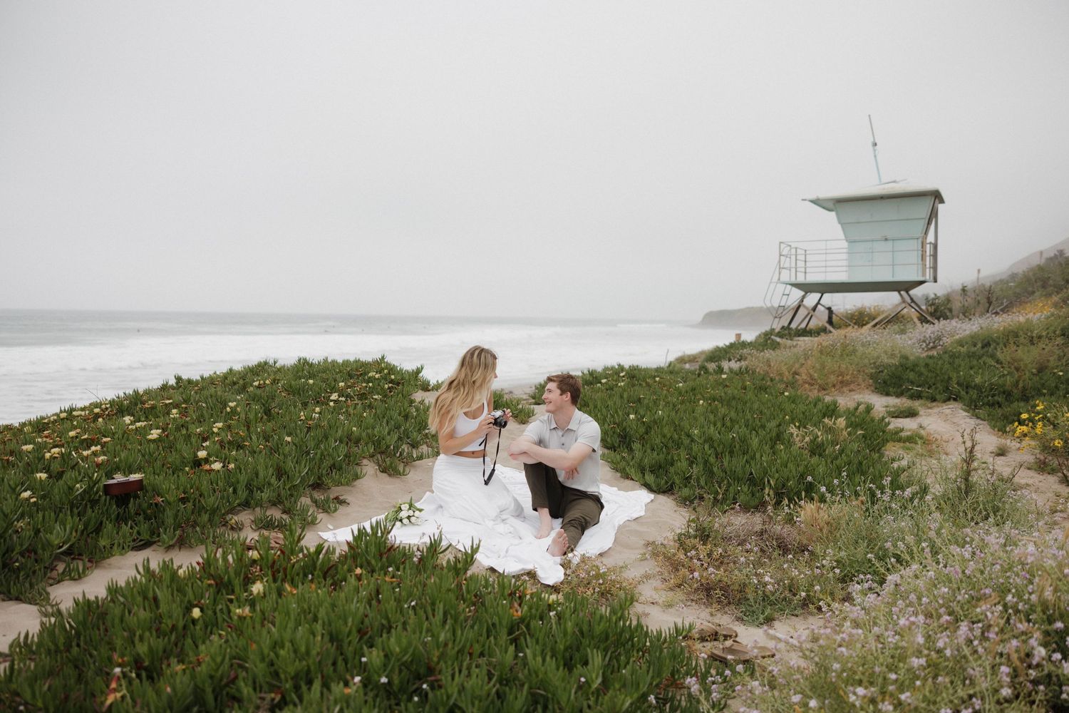 Couple having picnic on grassy coastal bluff near lifeguard tower.