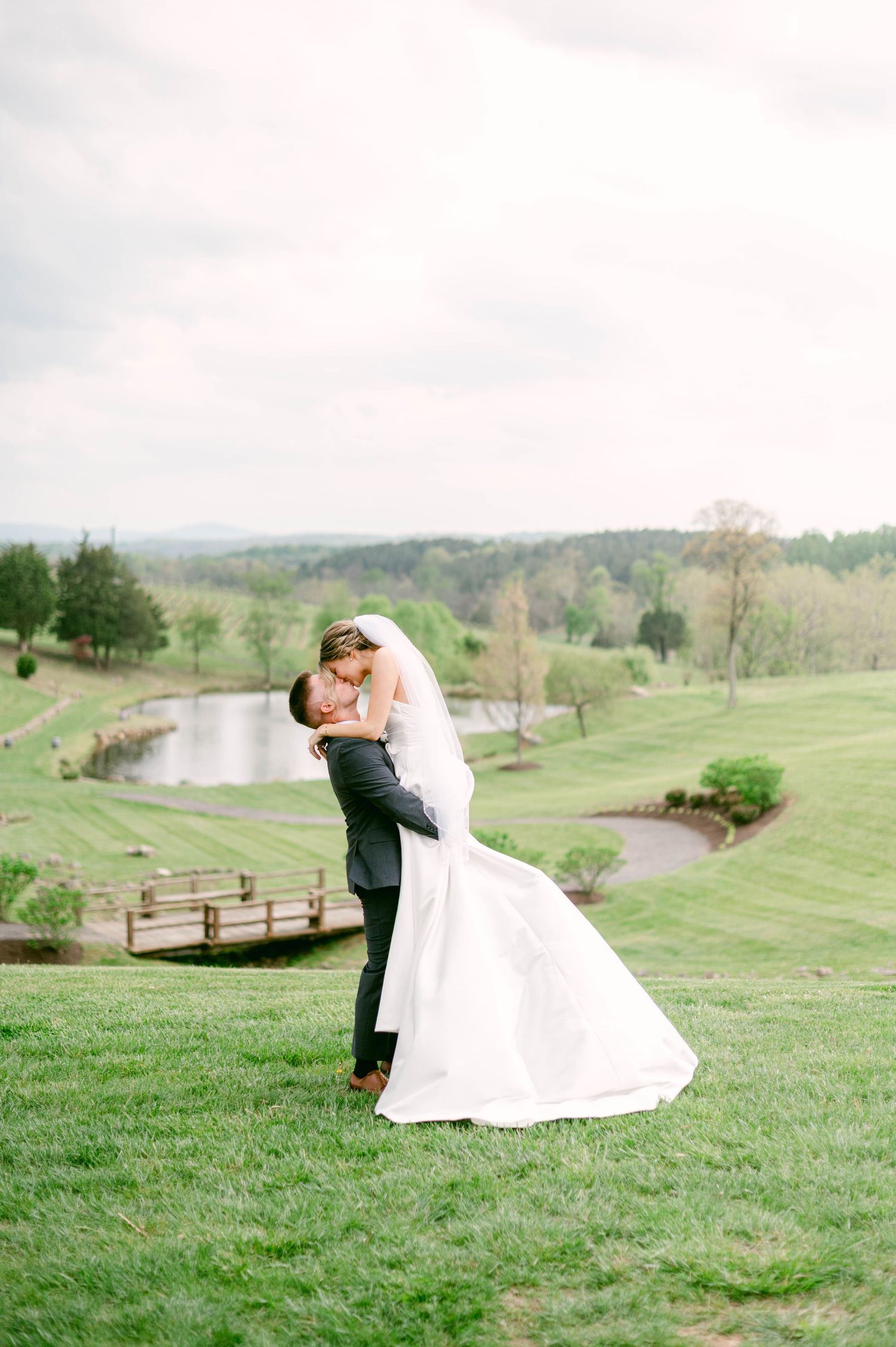 Romantic wedding couple shares intimate moment on rolling green hillside overlooking scenic landscape at Stone Tower Winery.