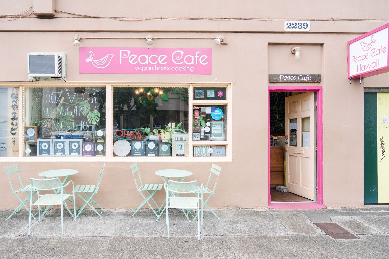 A pastel pink storefront of a French cafe with mint green outdoor seating and window displays of goods.