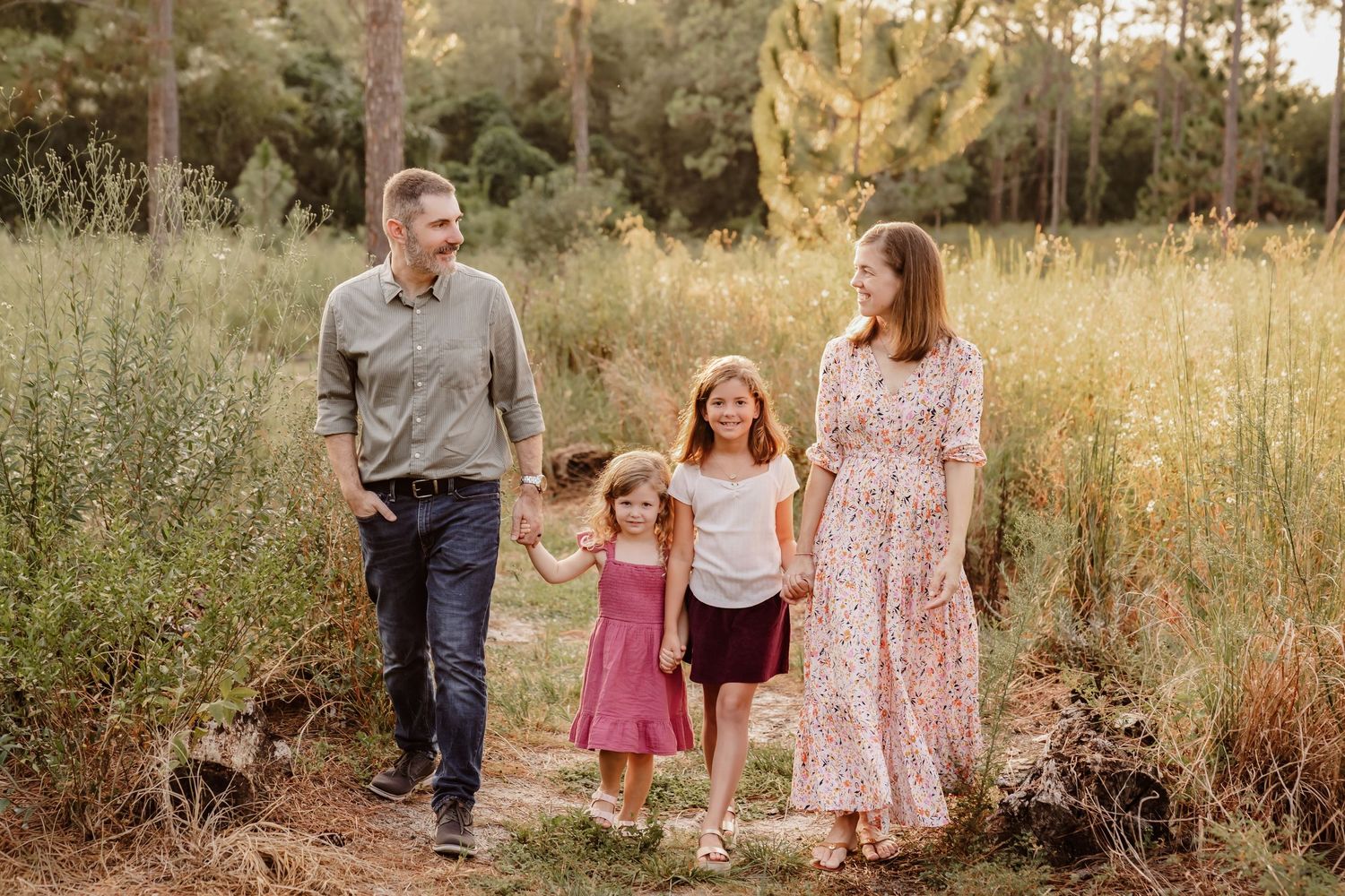 Family walking together through a golden sunlit meadow during sunset in casual outdoor attire.