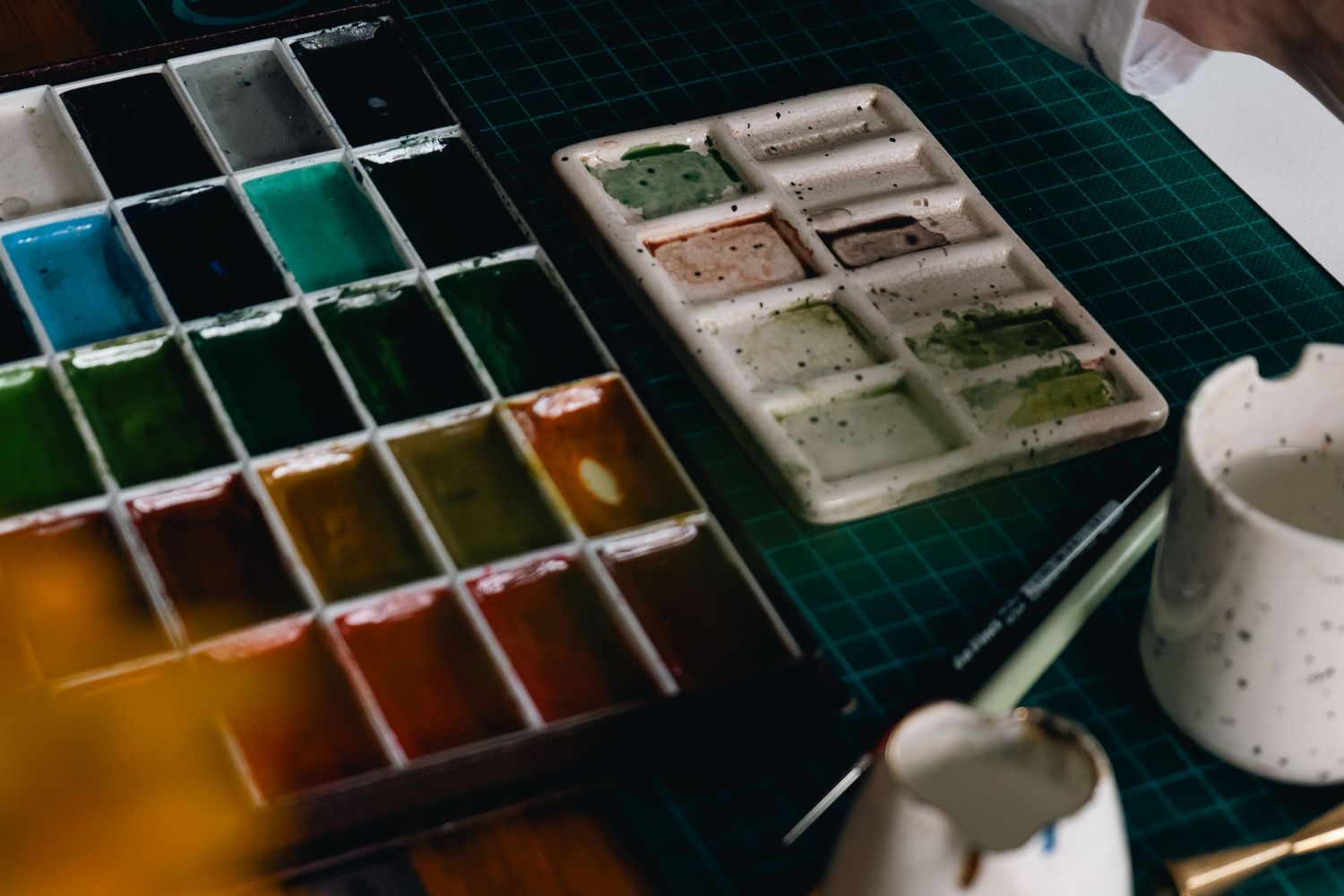 Watercolor paint palette with multiple colours being mixed on a dark green surface.