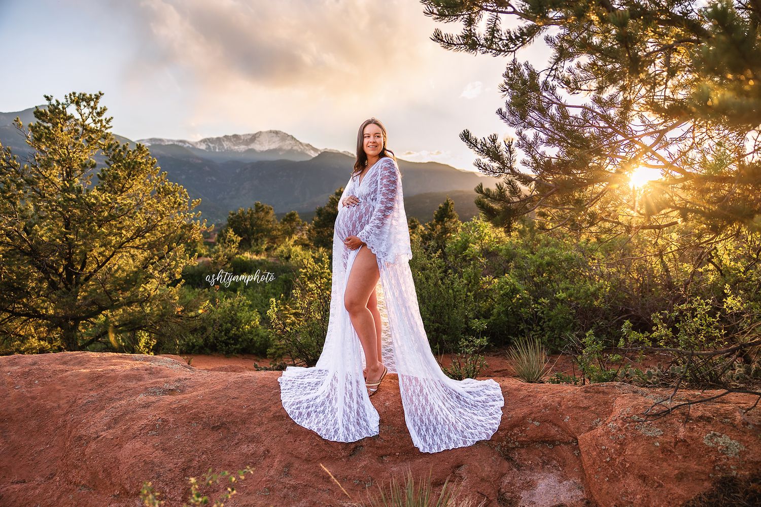 A flowy white lace dress cascades down red rocks at sunset with mountain peaks in the background.