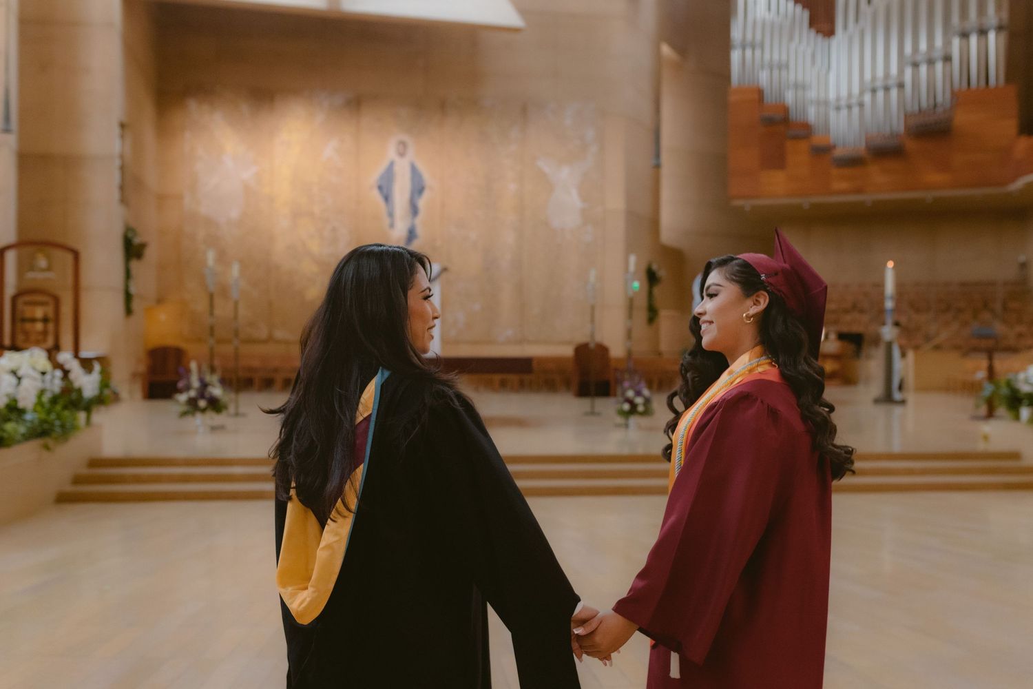 Two people stand in conversation inside a church-like space with wooden walls and an organ pipe display behind them.