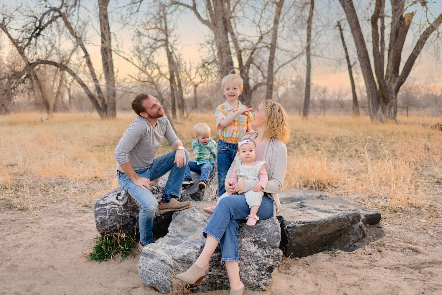 Family of 5 sat on rocks outside, mom has baby girl on her knee, toddler in middle at back, dad and mom looking at boy