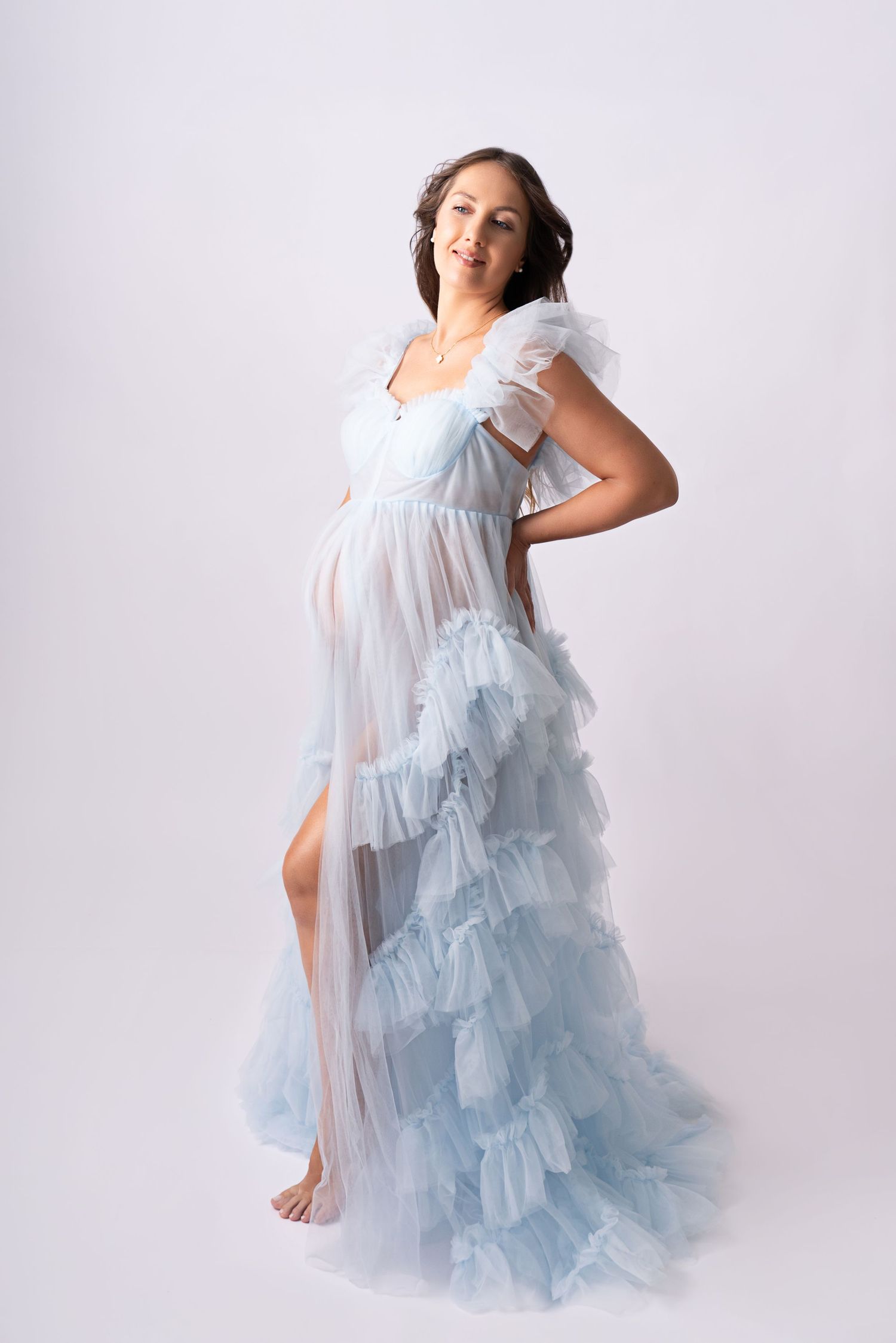 Ethereal light blue sheer maternity gown with ruffled tiers and flutter sleeves photographed against white background.