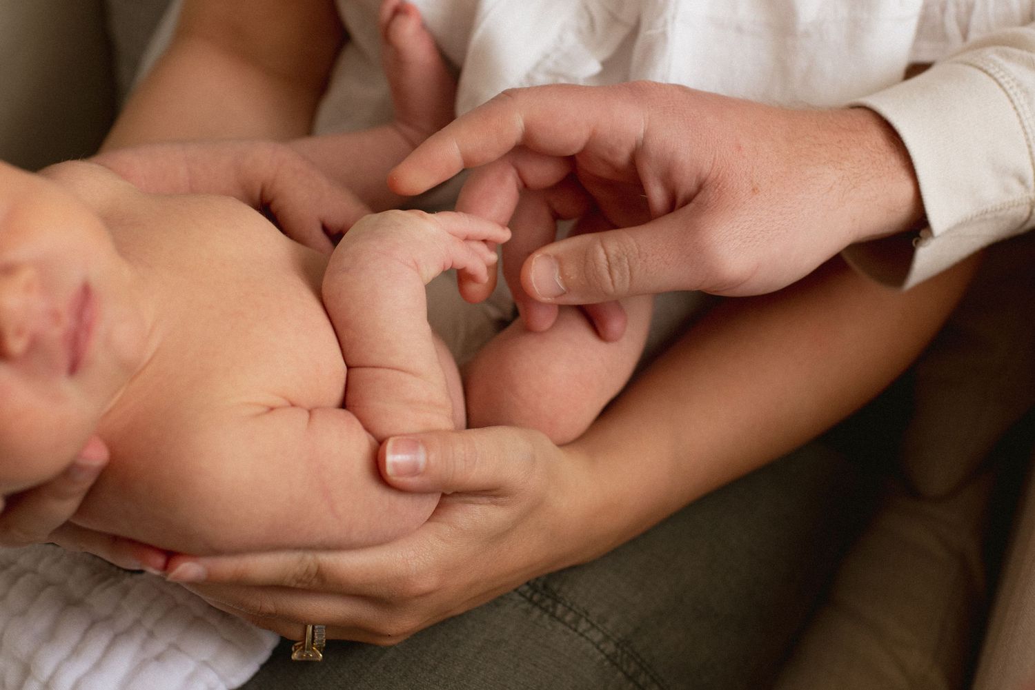 Adult hands tenderly holding baby's tiny fingers in close up view against soft fabric background.